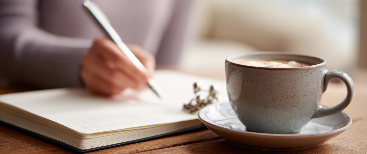Notebook open on a wooden table beside a cup of coffee, creating a calm, reflective moment with space to pause.