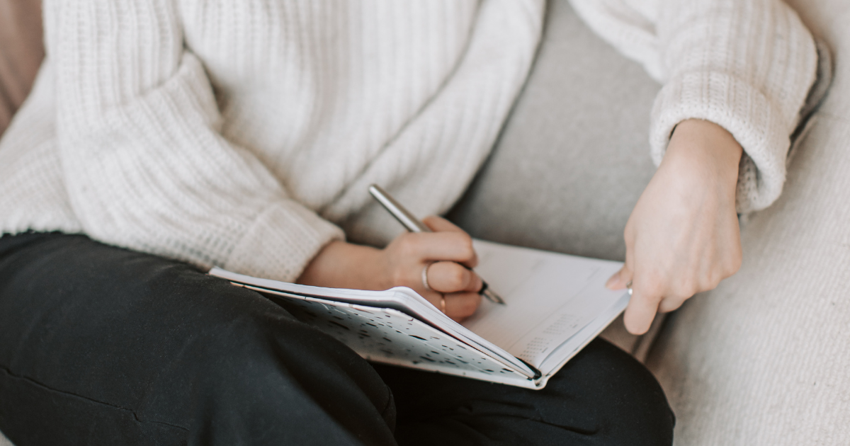 A woman writing in a diary while sitting on a sofa, holding a pen and gently planning the year ahead.