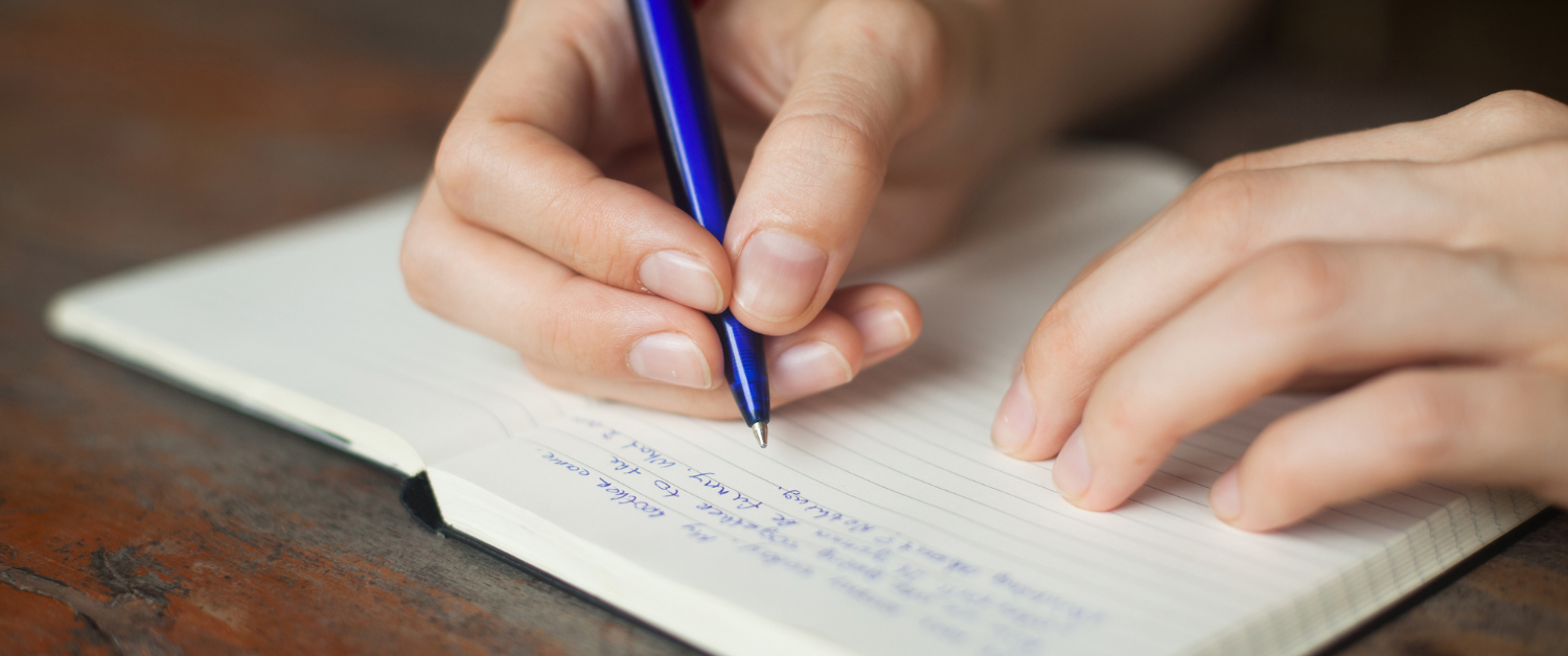 Hands writing in a notebook with a pen, capturing a quiet moment of reflection and intention-setting.