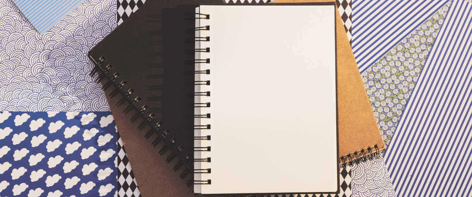Stack of blank notebooks with patterned covers, open empty page, suggesting a fresh start and gentle reflection.