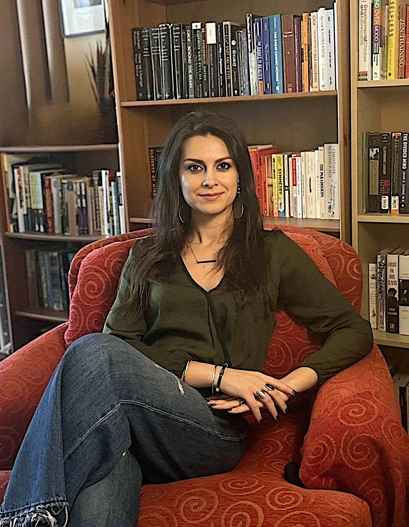 Giulia Davis, LMFT, seated in a red chair in front of a bookshelf, representing holistic psychotherapy.