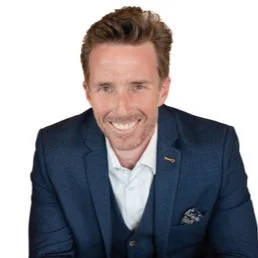 Smiling man in a blue suit with a white shirt, against a white background.