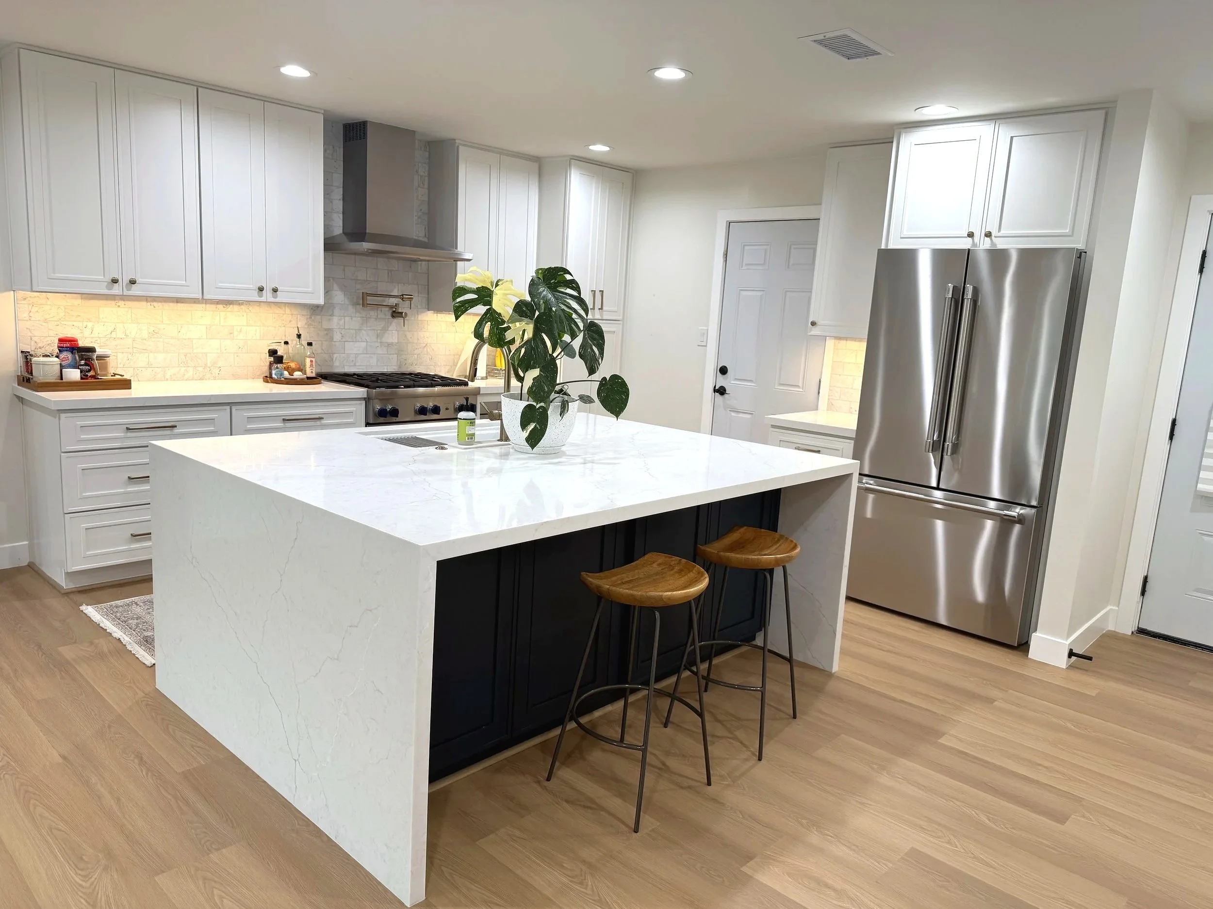 Modern kitchen with gray cabinets, white quartz countertop island, stainless steel appliances, and patterned tile backsplash.
