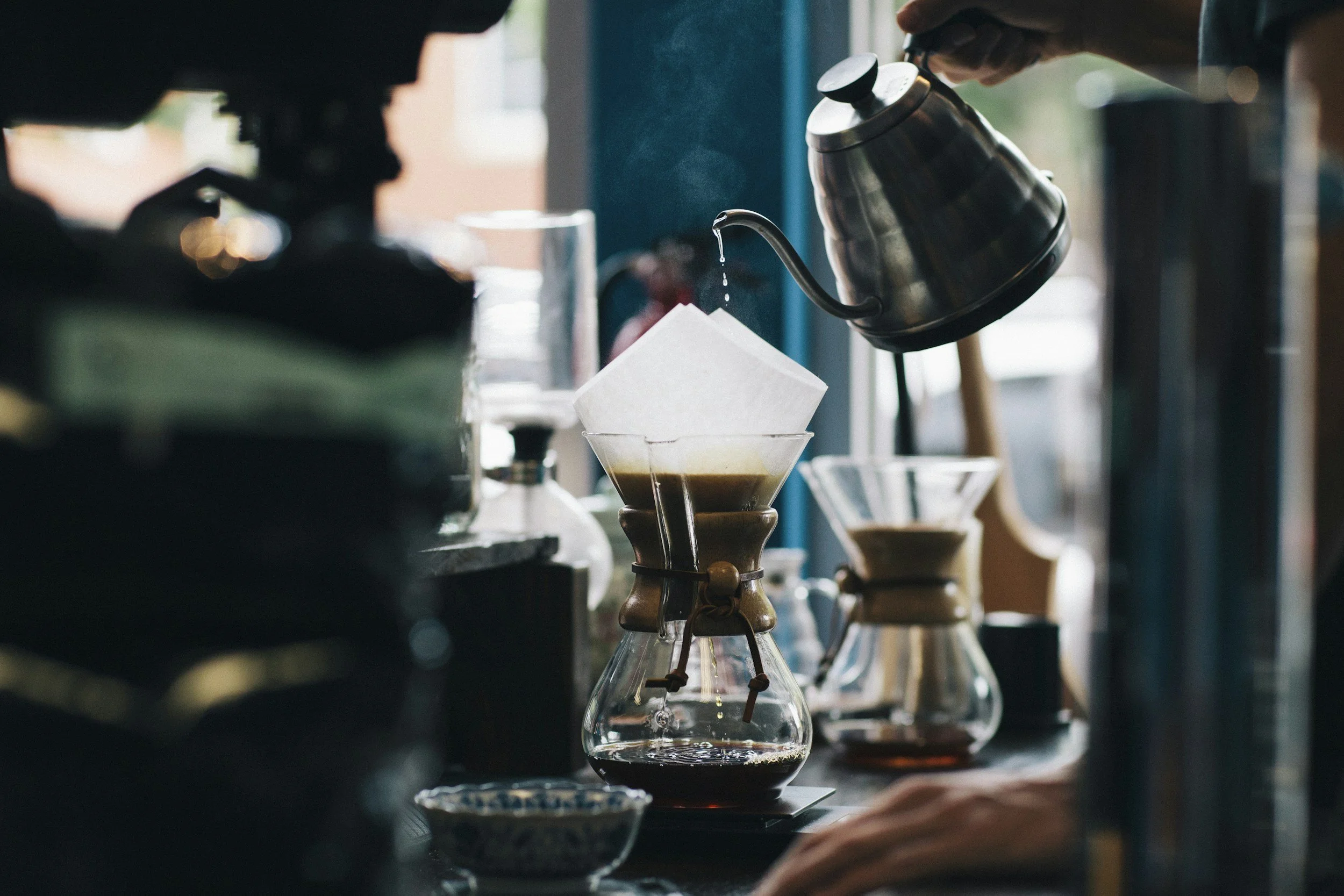 Person pouring hot water through a coffee filter into a glass coffee cone on a countertop.
