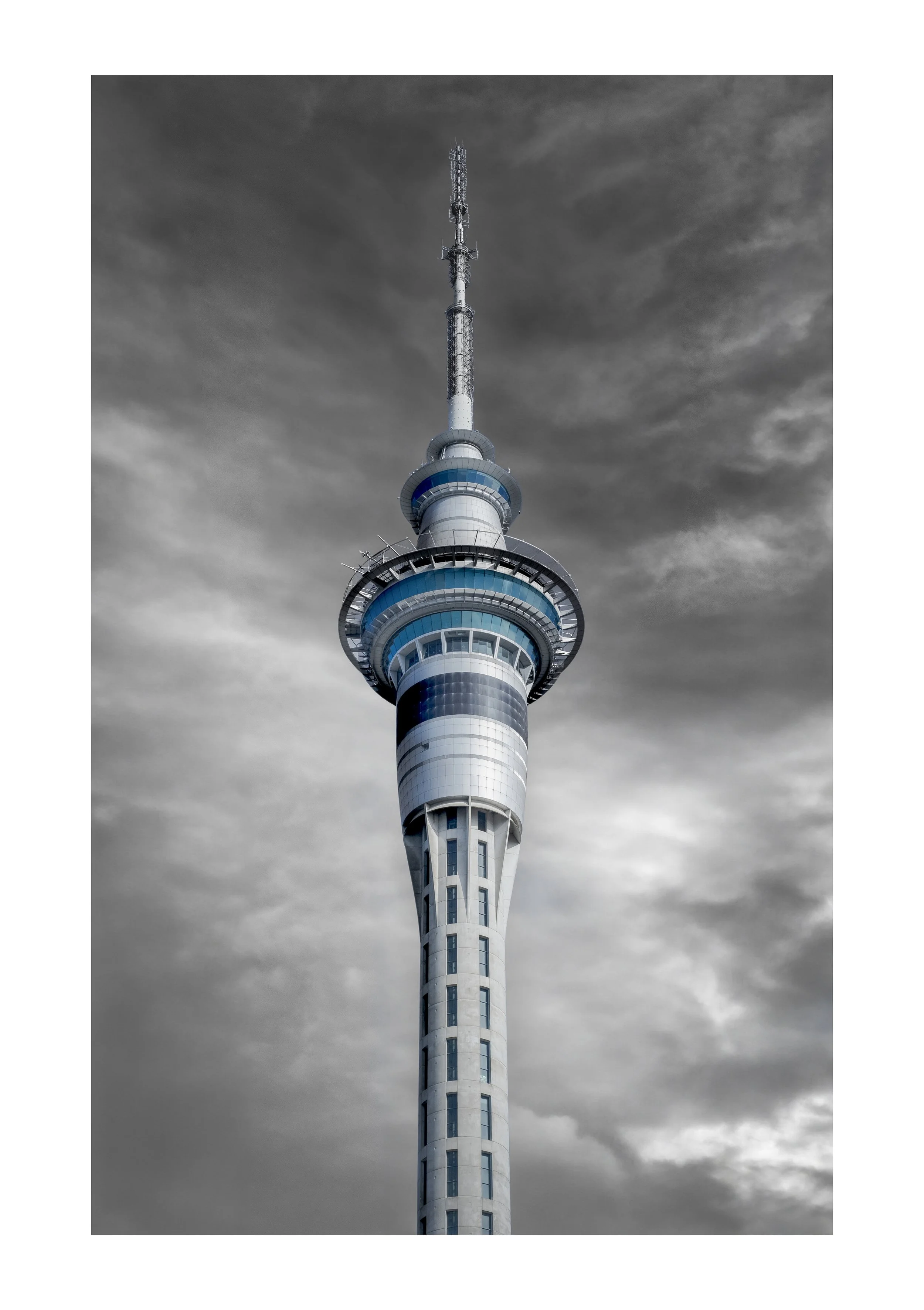 The Sky Tower Auckland New Zealand with blue and white geometric design against dark, cloudy sky.