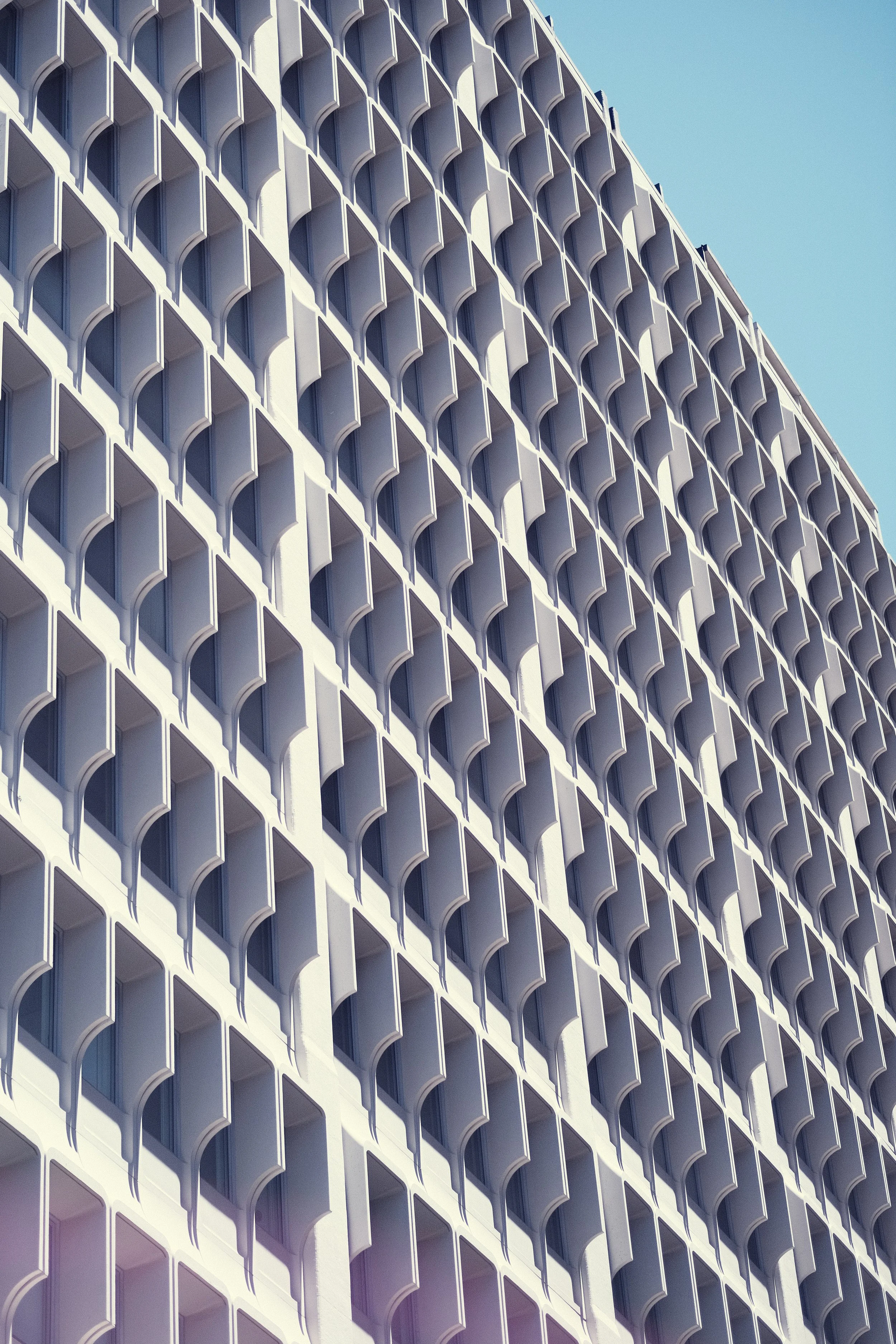A modern white building with a repeating geometric pattern of square balconies with curved edges, set against a clear blue sky.