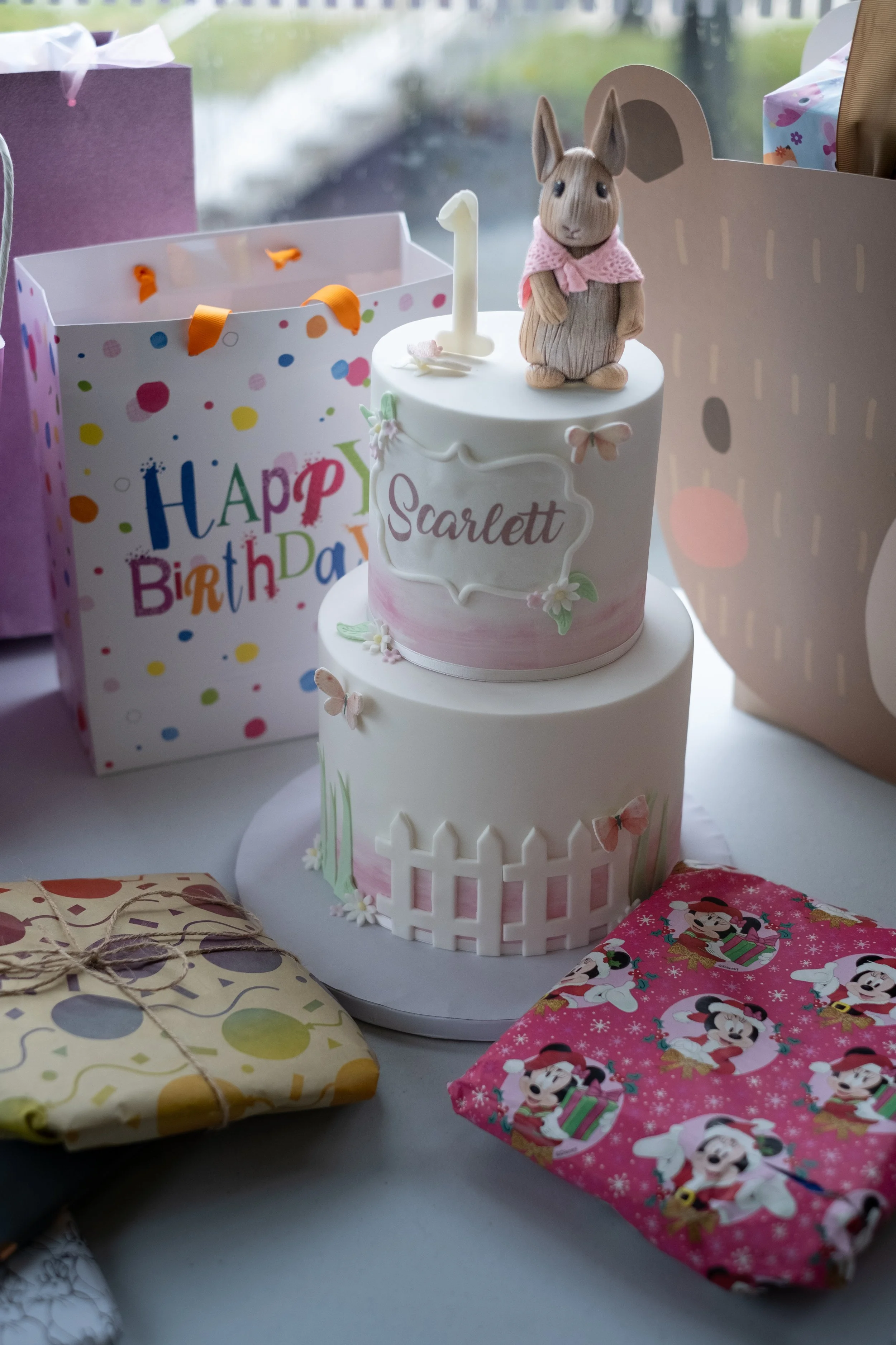 A birthday cake with a bunny figurine on top, surrounded by gift boxes with various patterns, including birthday and holiday themes.