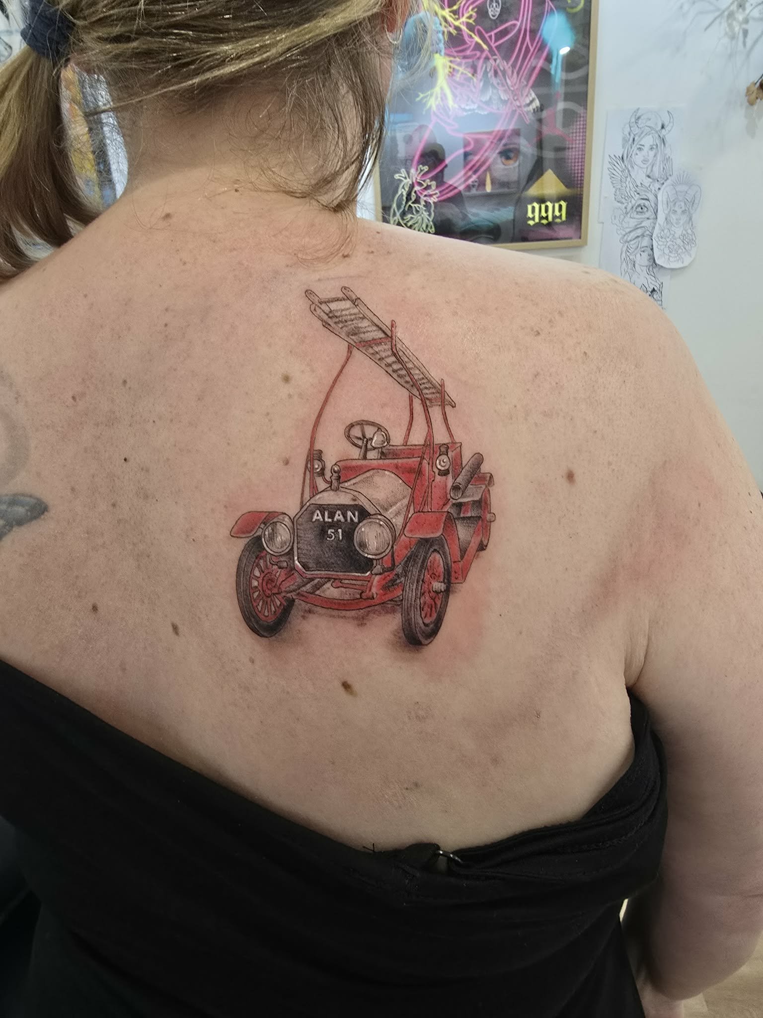 Tattoo of an antique red car with the name 'ALAN' and the number '51' on the front, located on a person's upper back and shoulder.
