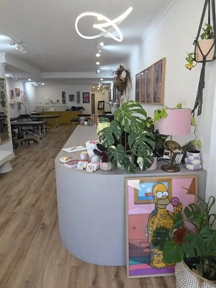 Interior of a modern art or design studio with a reception desk, green plants, artwork on the walls, and decorative items, including a Homer Simpson portrait.