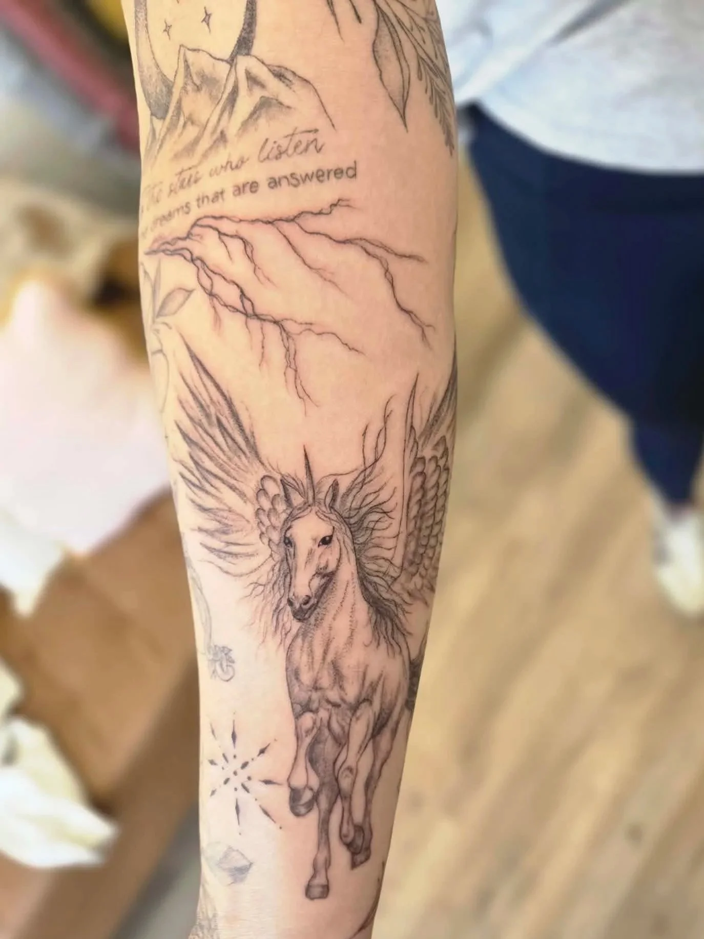 Tattoo of a winged horse running, with detailed wings and flowing mane, on a person's arm. Tattoo of a roamtasy novel, fantasy novel inspired tattoo, illustrative tattoo design, custom fantasy book theme tattoo.