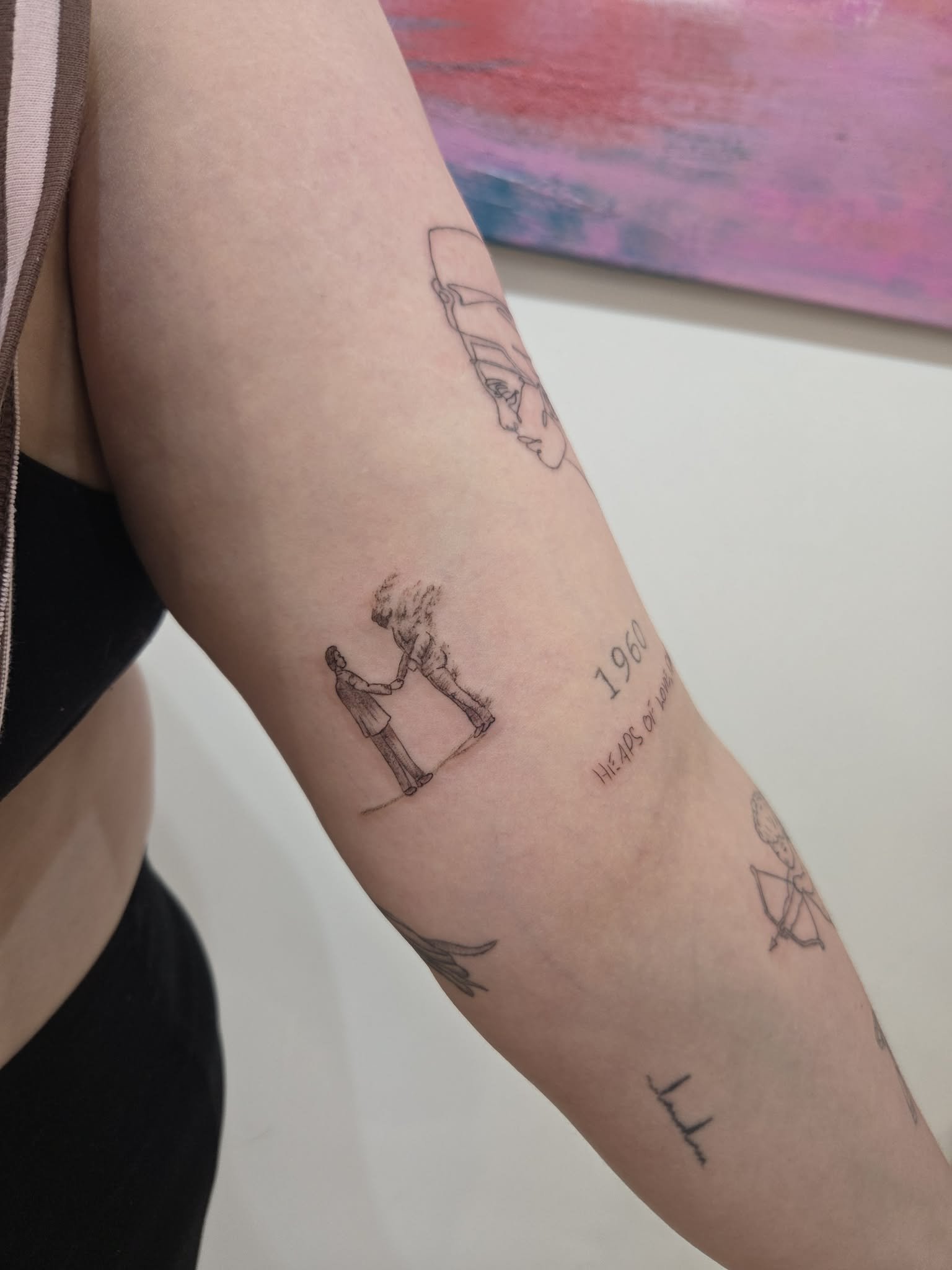 Tattoos on a person's arm, including a line drawing of a face, two figures shaking hands with a cloud above, the year 1960, and various other sketches and text. Delicate fine line rose tattoo by Melbourne tattoo artist at Heart and Home Tattoo studio