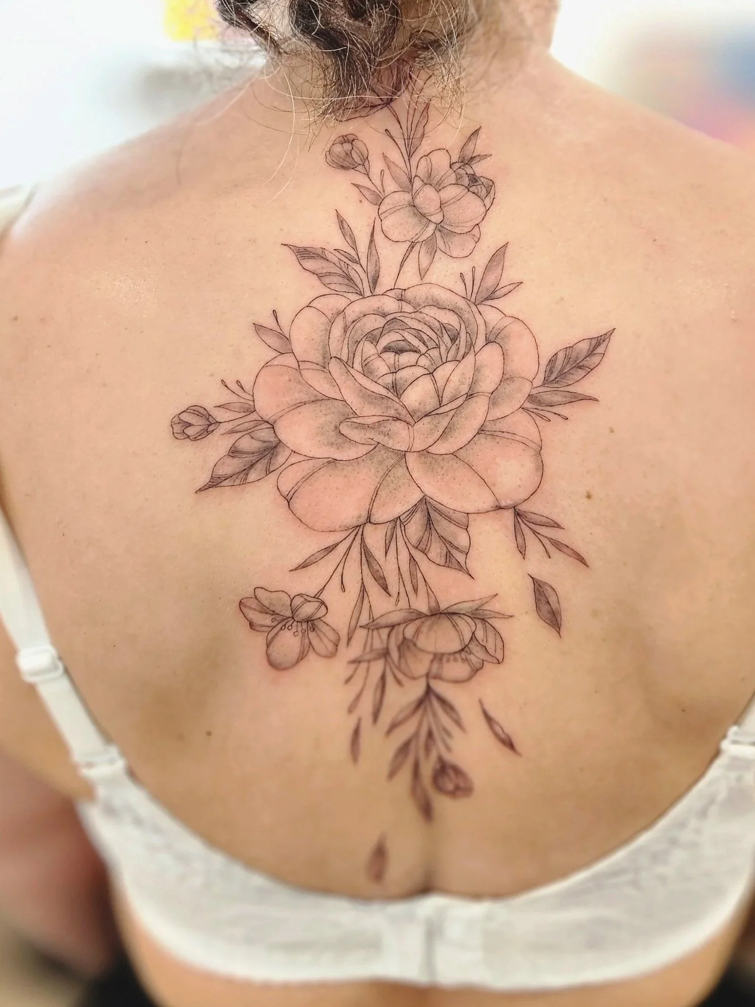 A person's upper back and shoulders with a large, intricate floral tattoo featuring roses, leaves, and smaller flowers.