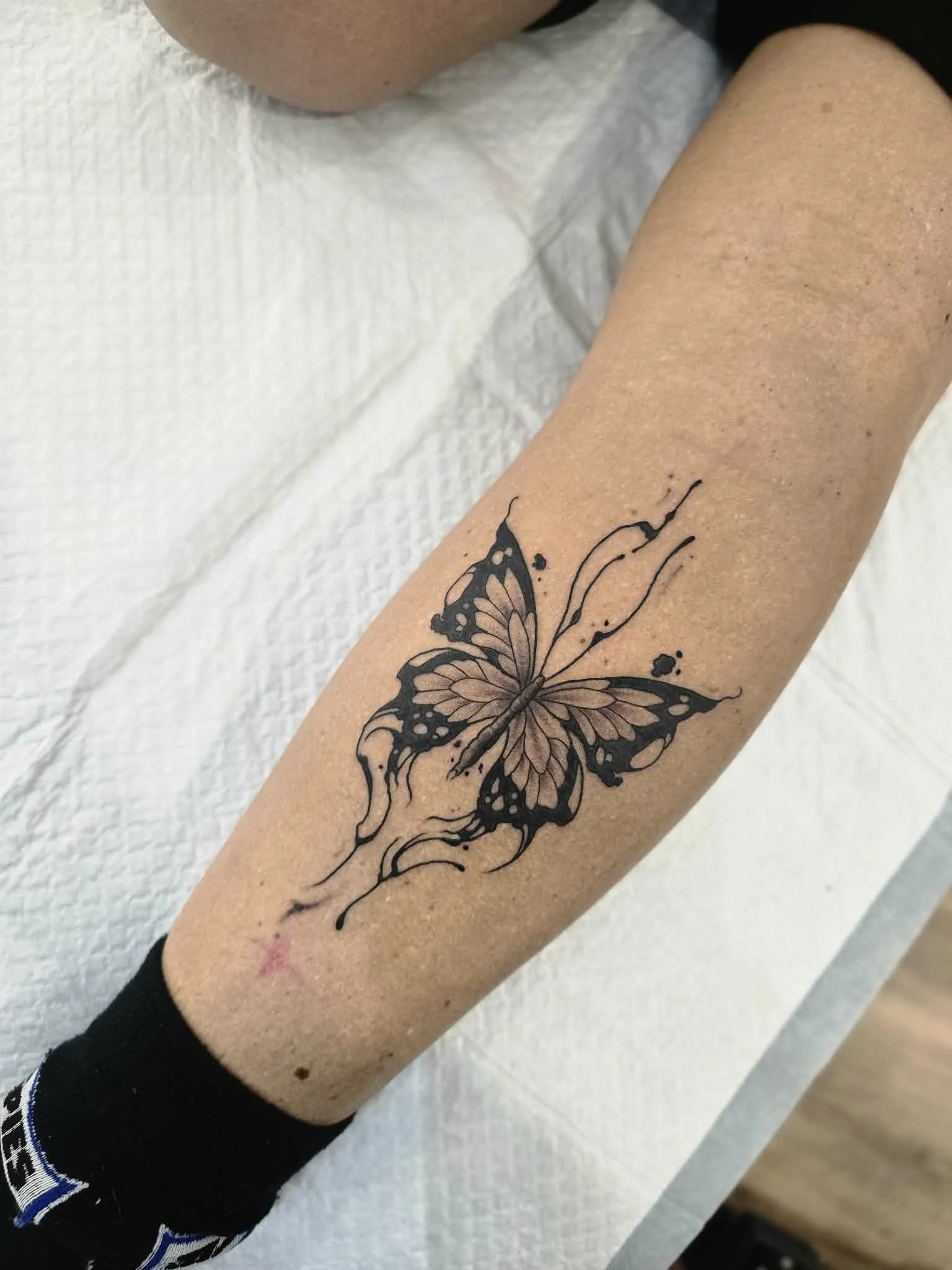 Black and grey butterfly tattoo on a person's forearm.