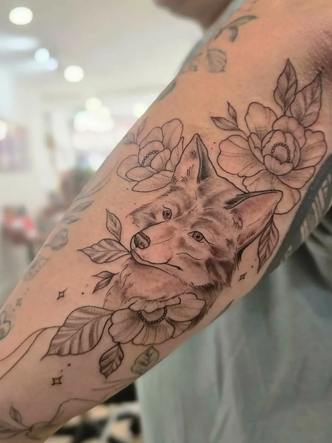 Tattoo of a wolf's face surrounded by flowers and leaves on a person's arm.
