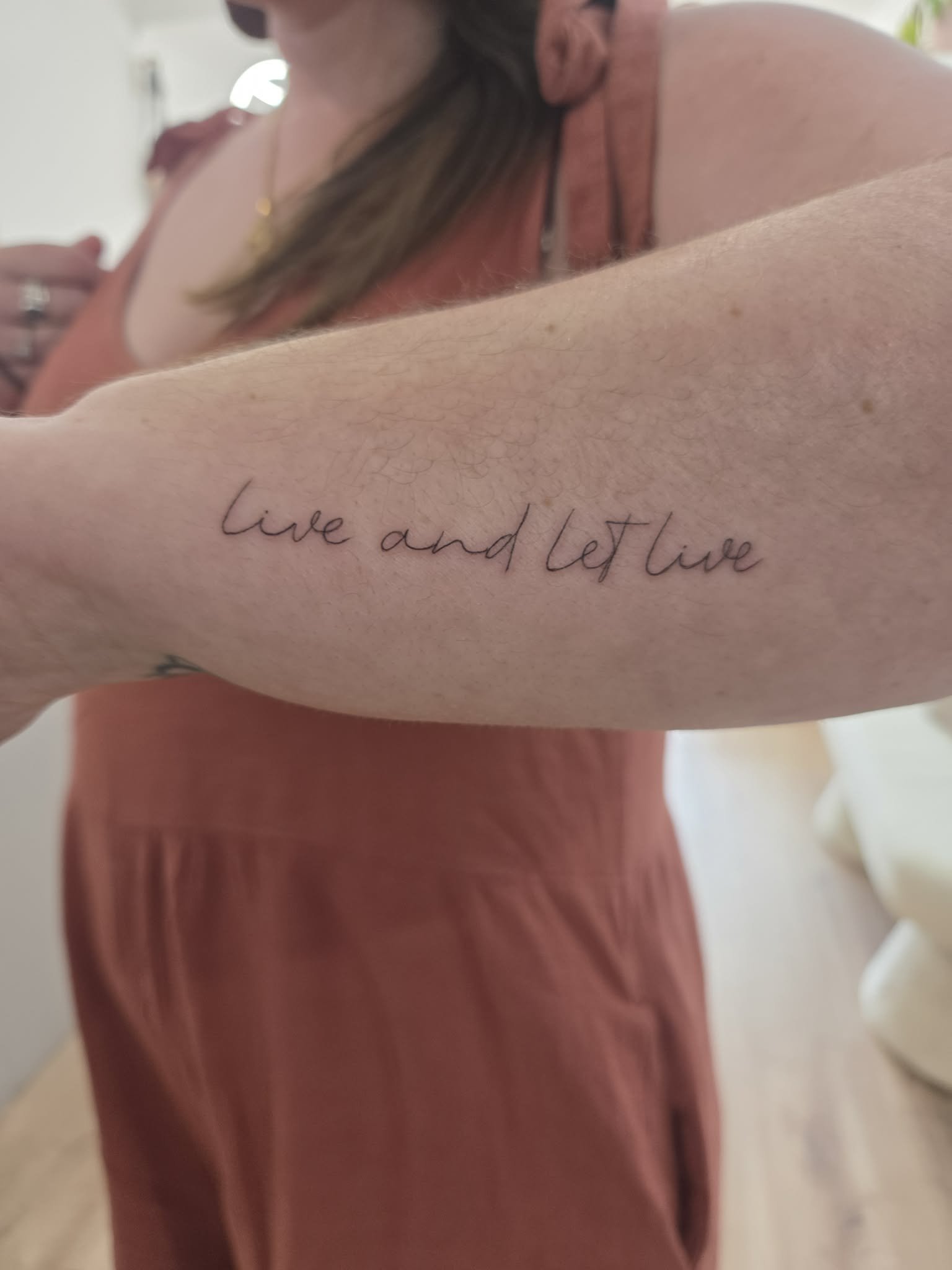 Close-up of a person's inner forearm with a tattoo that reads 'live and let live' in cursive script.