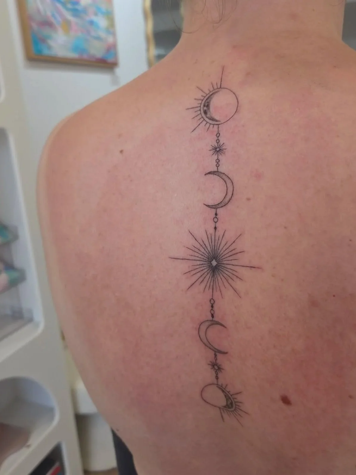 Tattoo of a celestial design with stars, moons, and sunbursts running vertically along the person's upper back.
