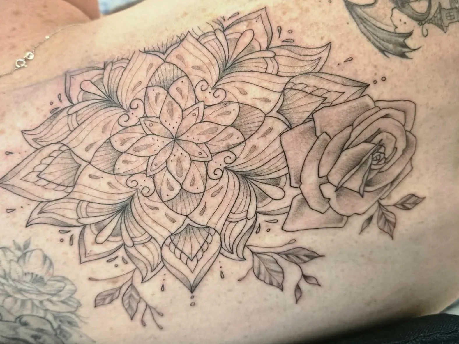 Tattoo sketch of a flower with intricate line details, surrounded by leaves and additional floral elements.
