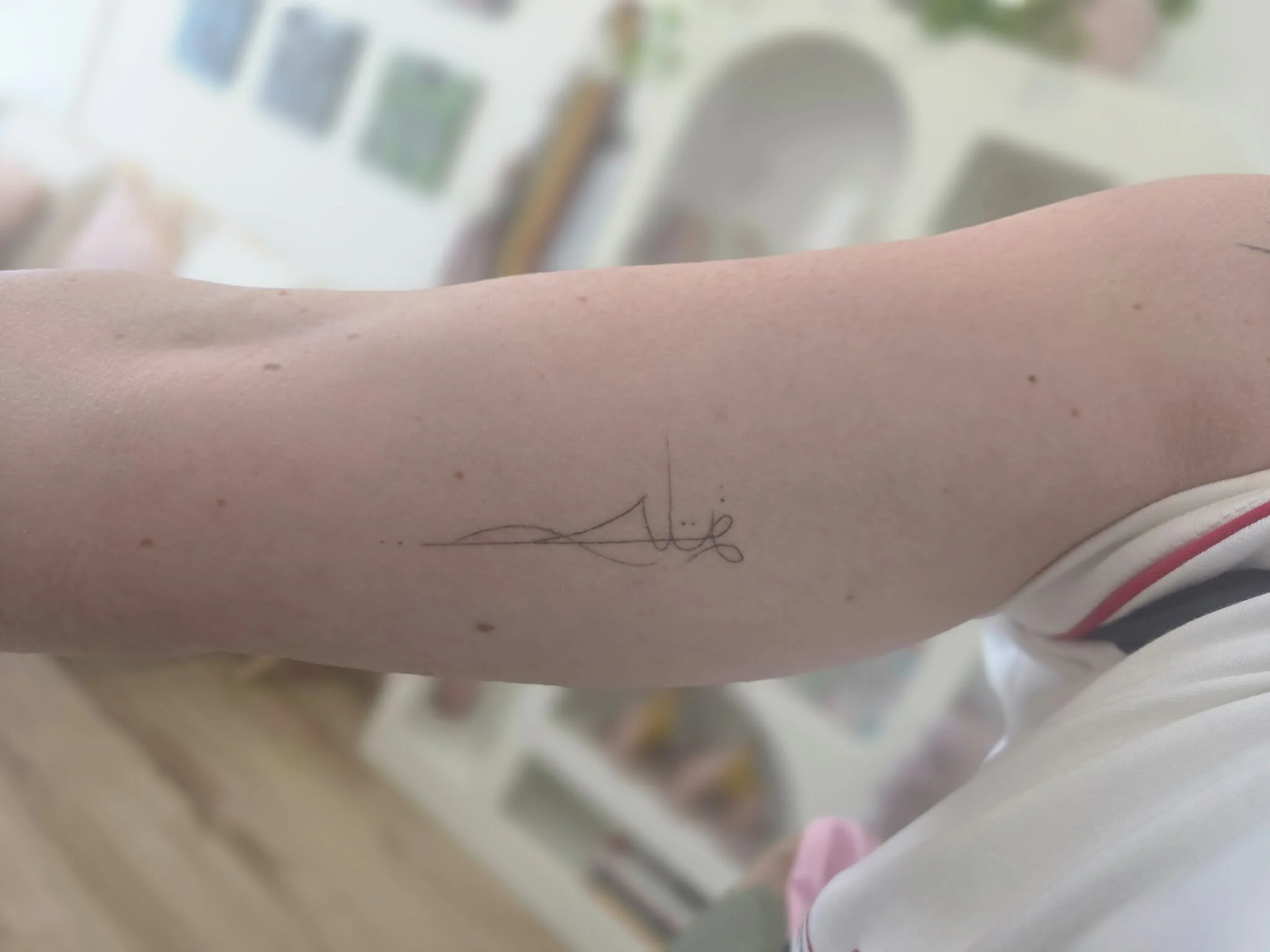 Close-up of a person's forearm with a small, simple, black ink tattoo consisting of a line and a signature.