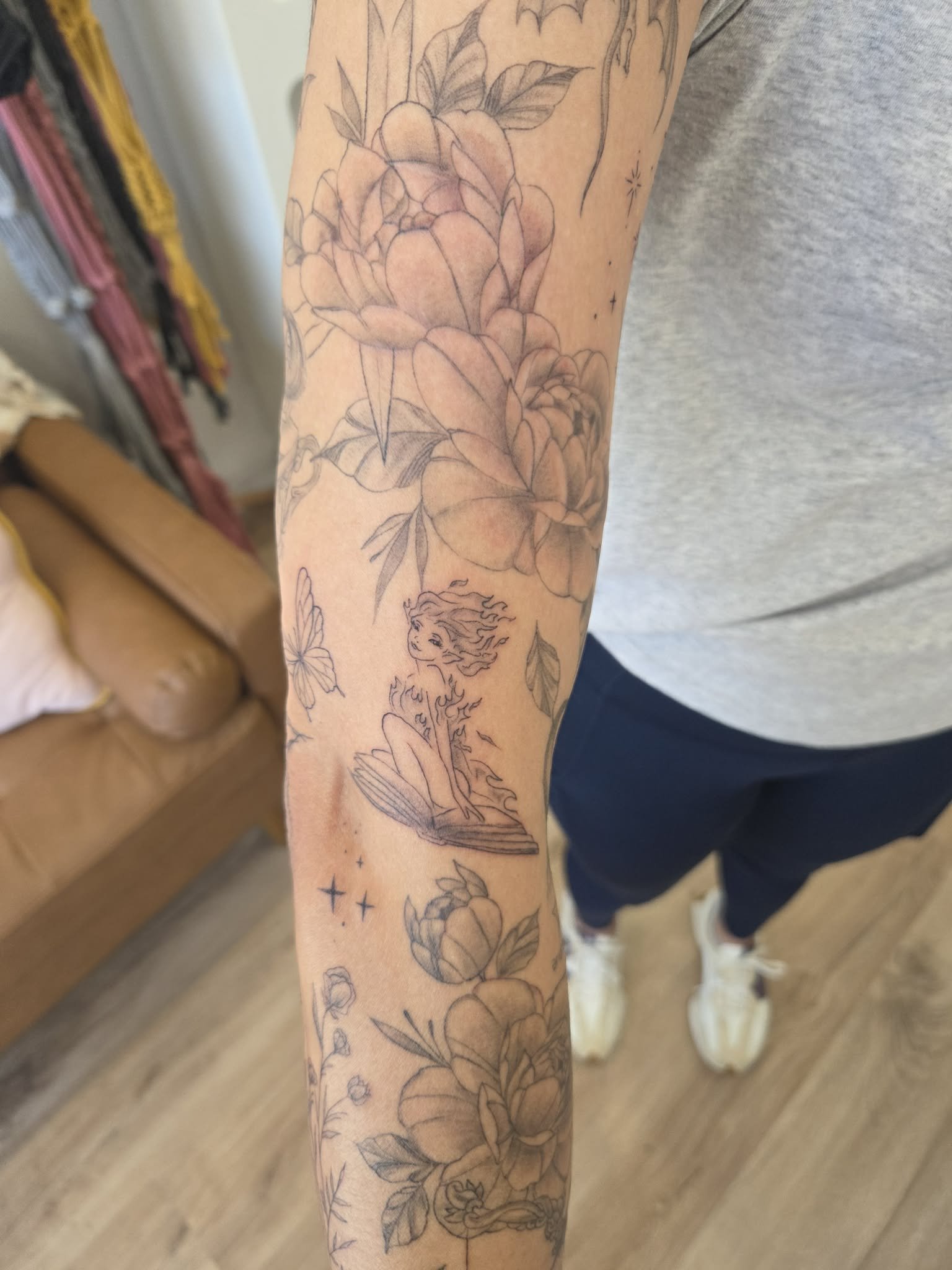 Line drawing of large flowers, a fairytale fairy sitting on a leaf with flowing hair, smaller flowers, stars, and other decorative elements on a person's arm.