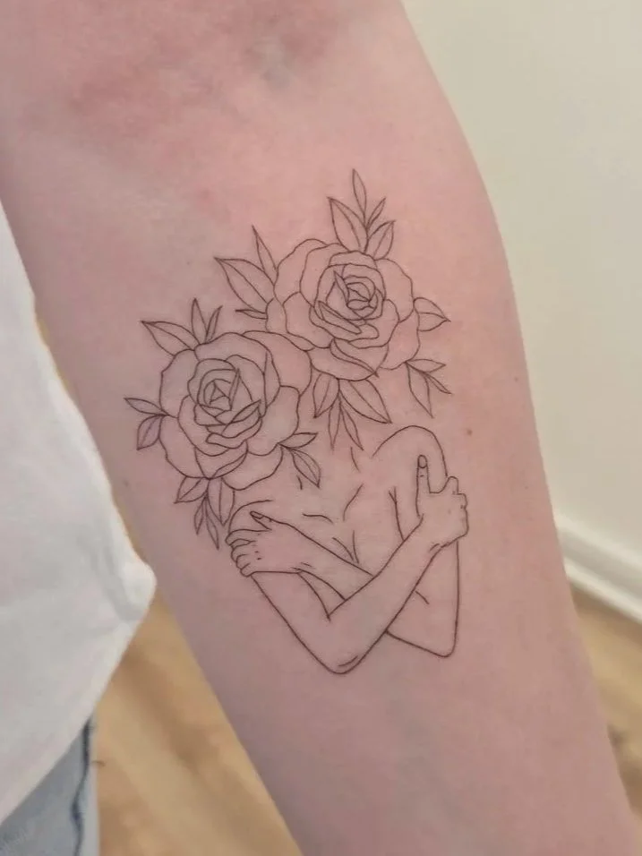 Tattoo of a woman hugging herself with her head replaced by two large roses and leaves. A Fine line tattoo with clean line work.