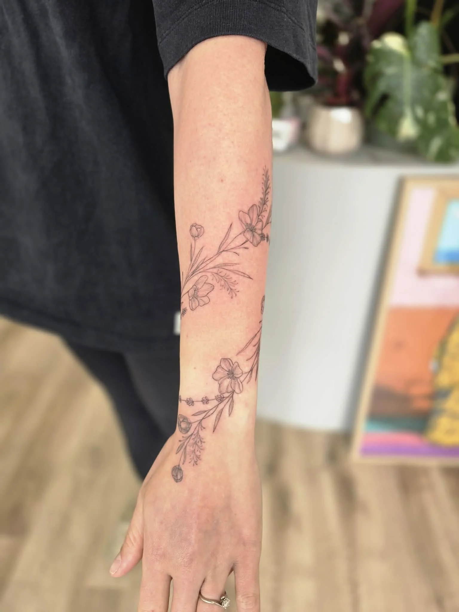 A person's arm with a line art floral tattoo, featuring flowers and leaves, on the forearm. Fine line rose tattoo by Heart and Home Tattoo, Moonee Ponds Melbourne