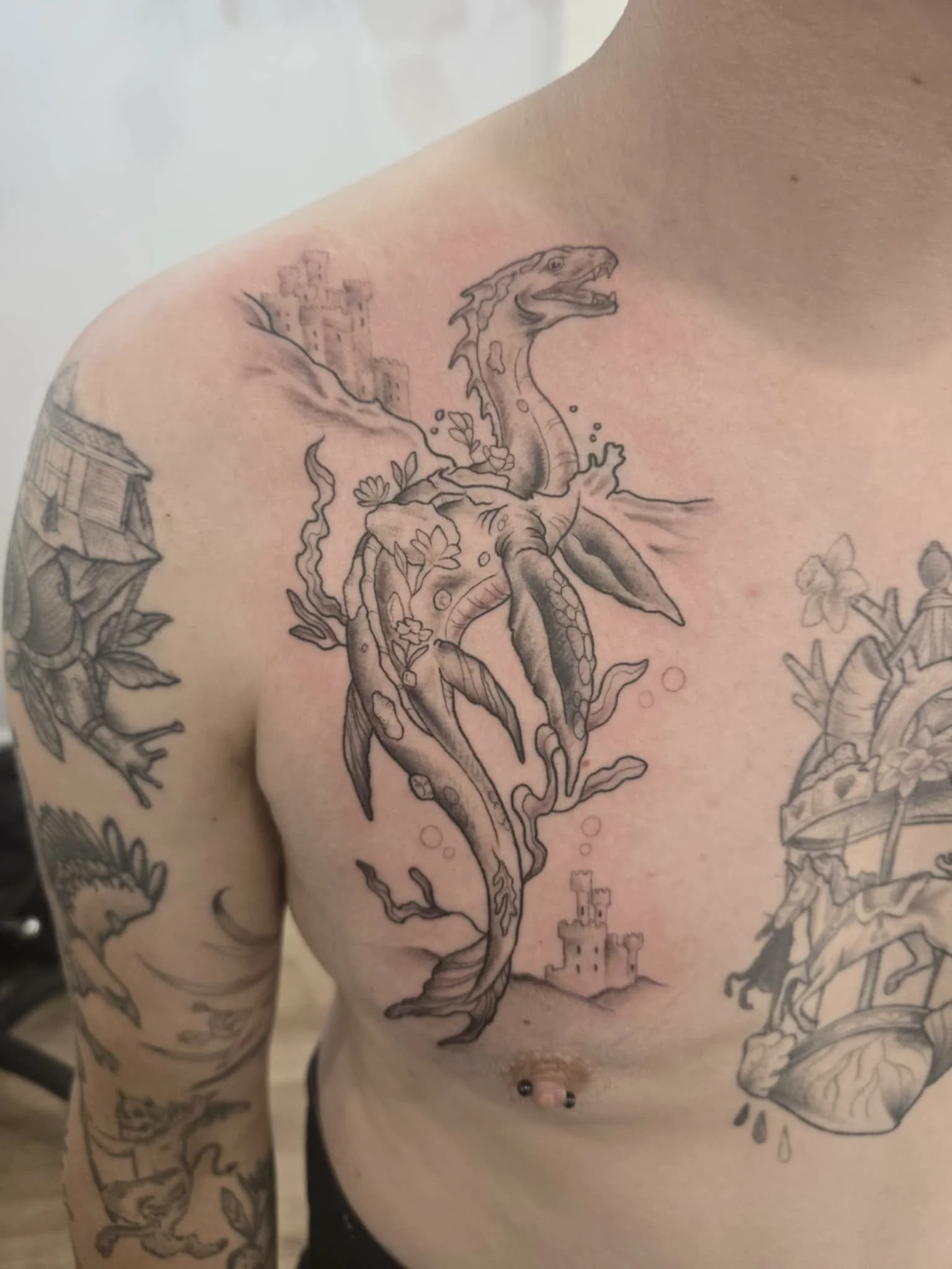 Black and gray tattoo of a dragon with castle in the background on a man's chest.
