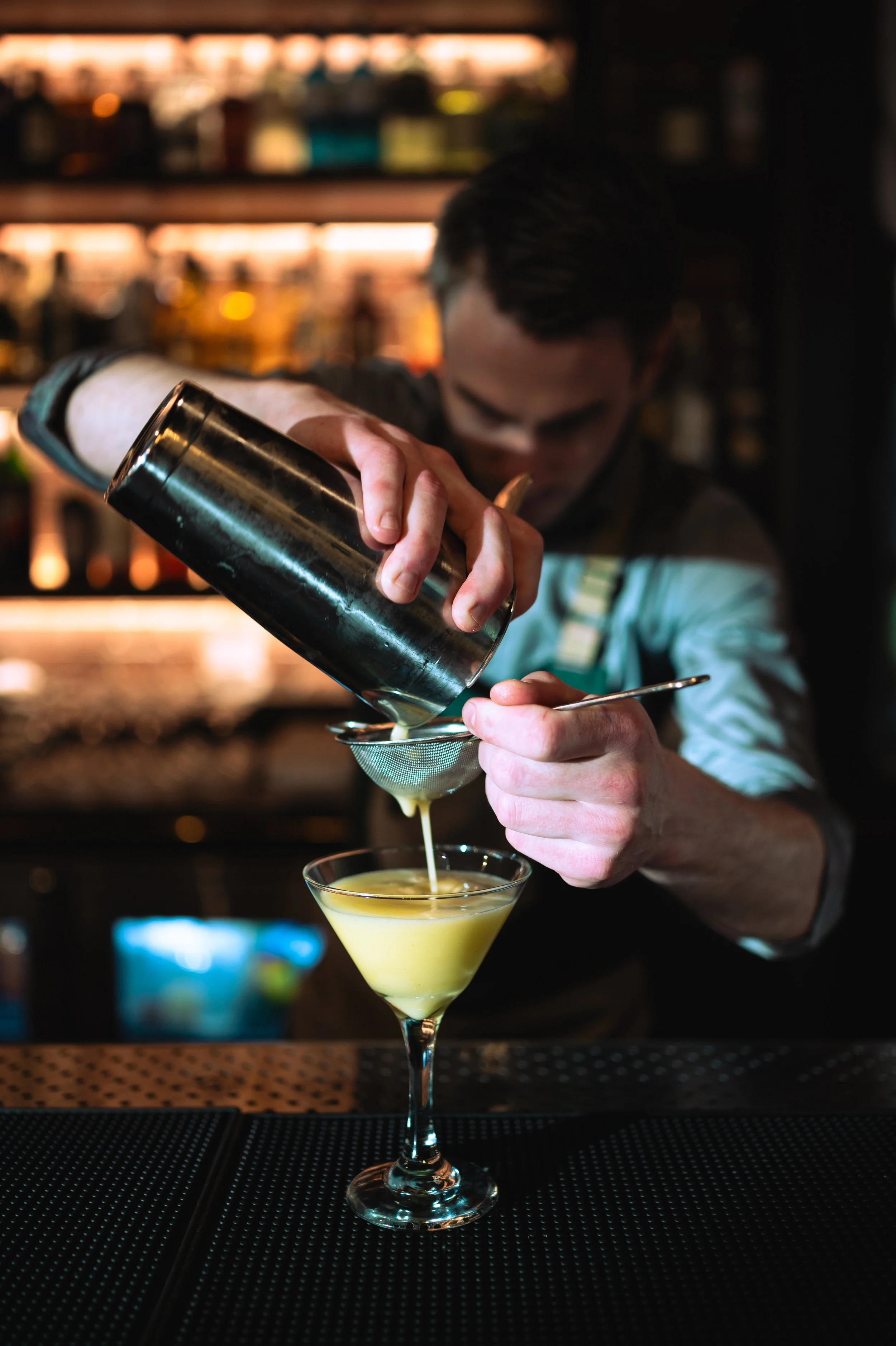 A photo of a bartender pouring a yellow cocktail through a strainer into a martini glass at Salt & Brick in Calgary