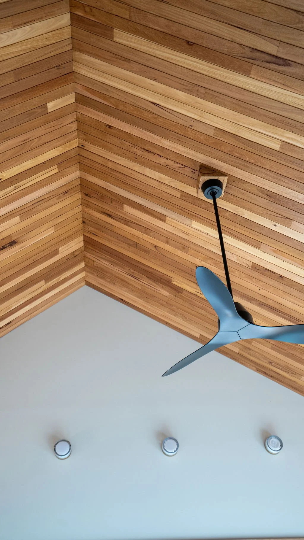 A ceiling with wooden paneling, a modern ceiling fan with three blades, and three recessed lights.