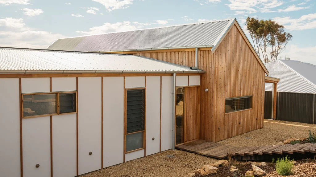 Modern house with a mix of white and wooden exterior, metal roof, and a small wooden deck in the backyard.