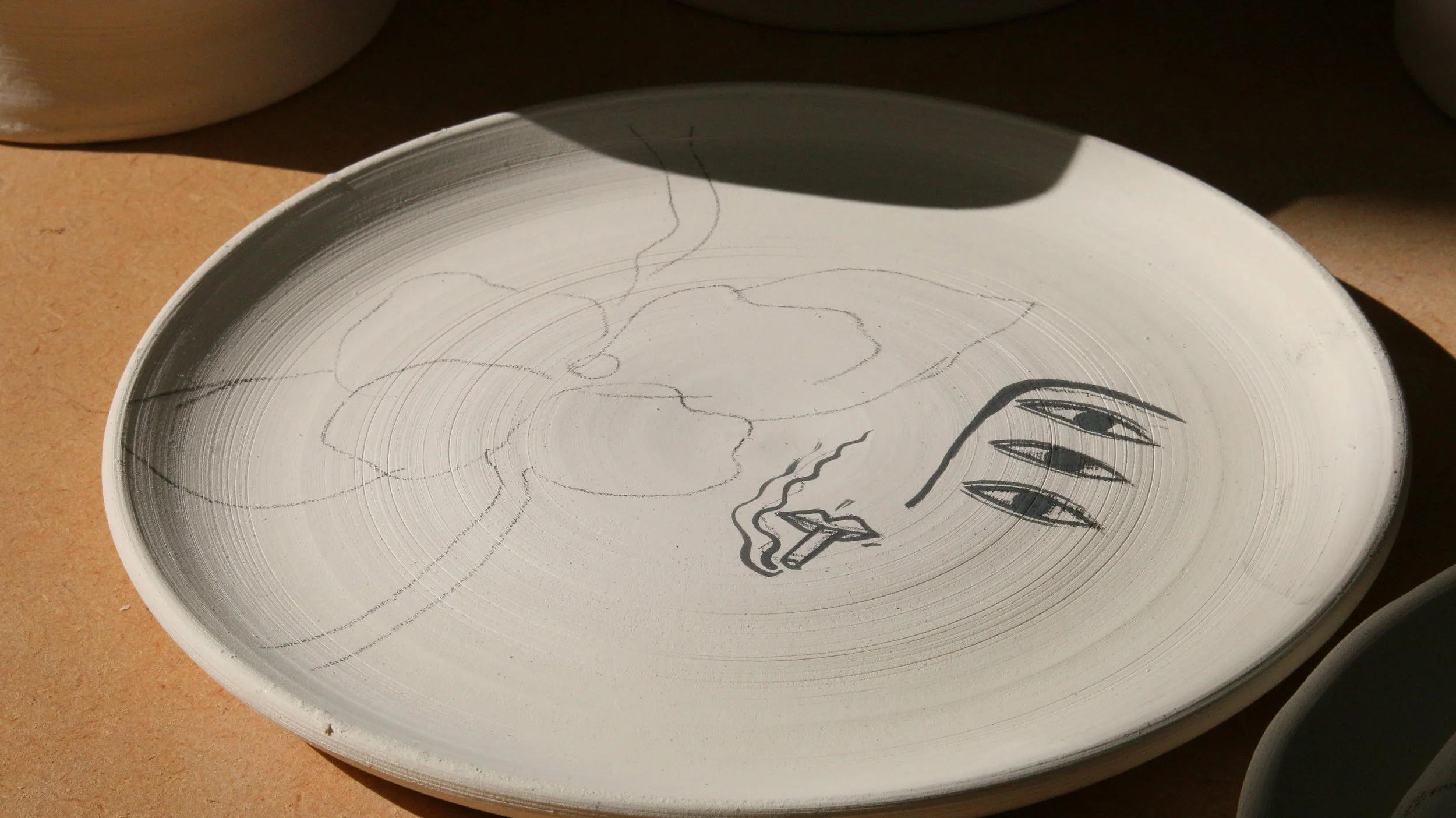 A ceramic plate with a hand-drawn design featuring a face with sharp teeth, eyes, and a flowing hairstyle, along with scribbled lines and shapes.