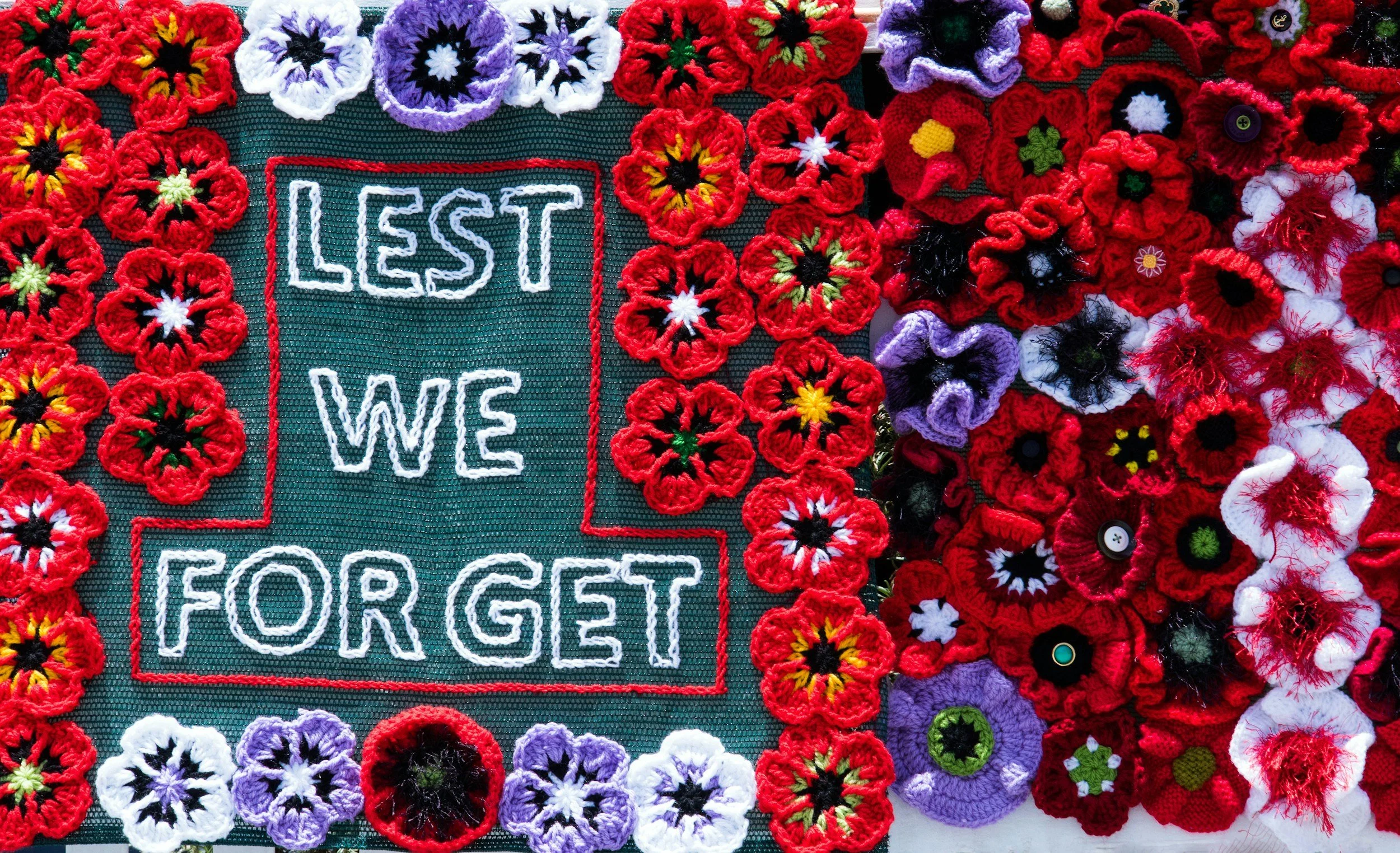 Knit flowers surrounding the phrase 'LEST WE FORGET' on fabric.