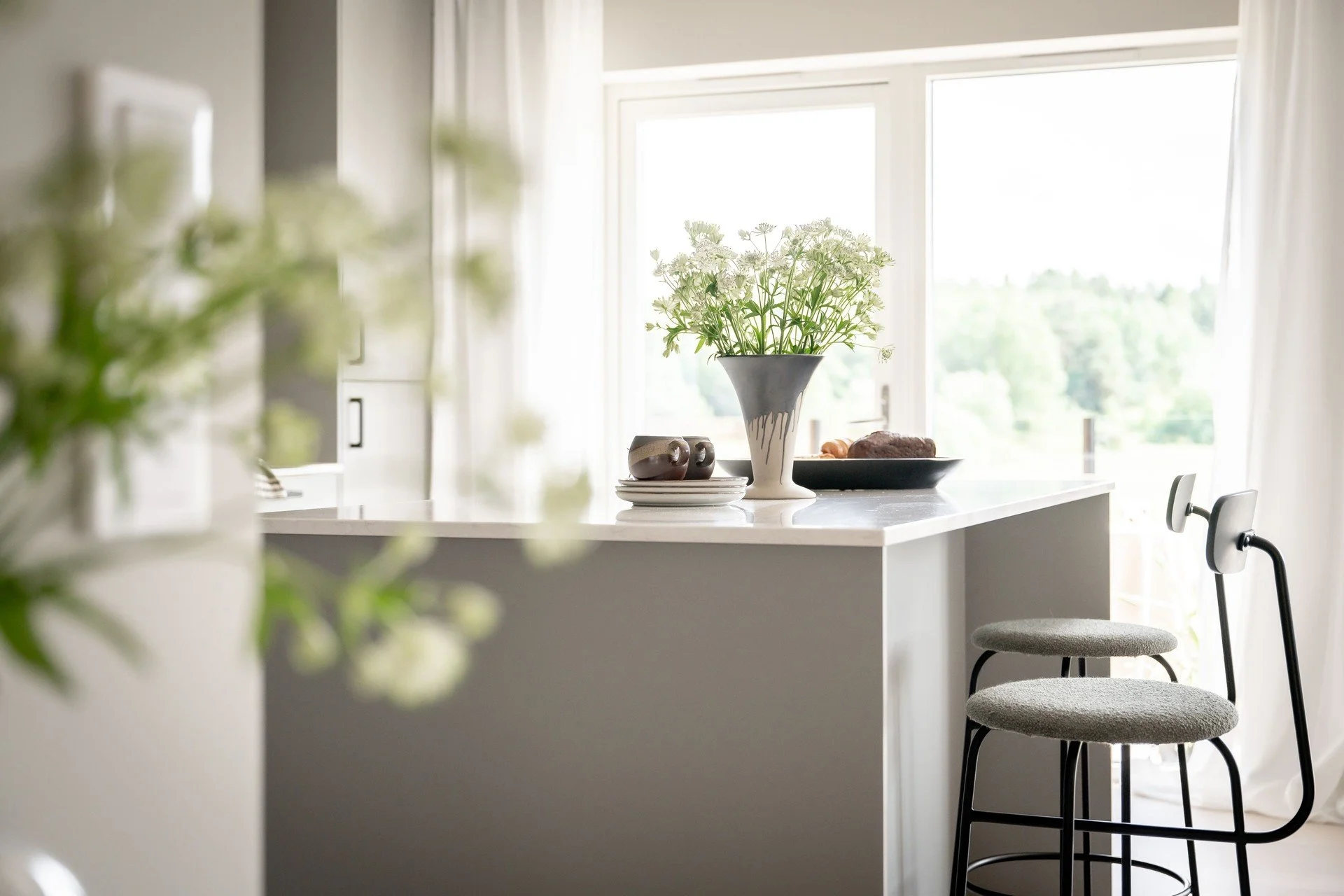 Modernt kök med bänk, barstolar och blommor i vas.