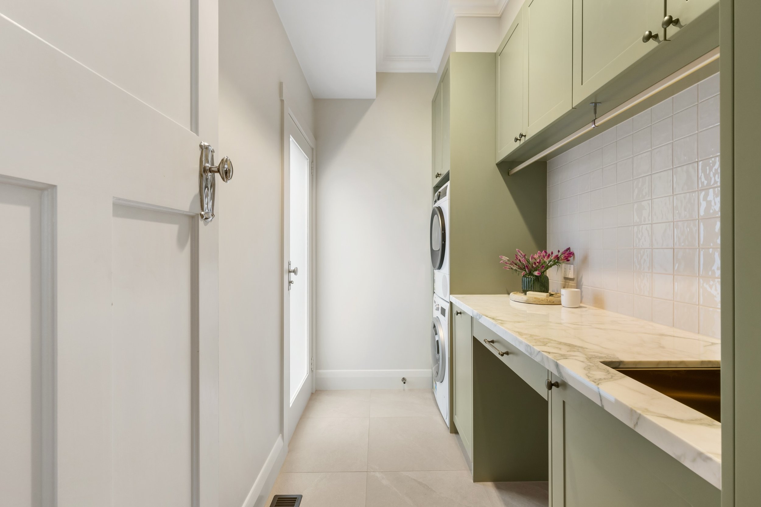 This beautiful laundry maximises functionality with added bench space, integrated washing basket, hanging rails, and a double-stacked washer and dryer. As well as a cosy nook for the family dog! 

This space incorporates custom cabinetry, bold materi