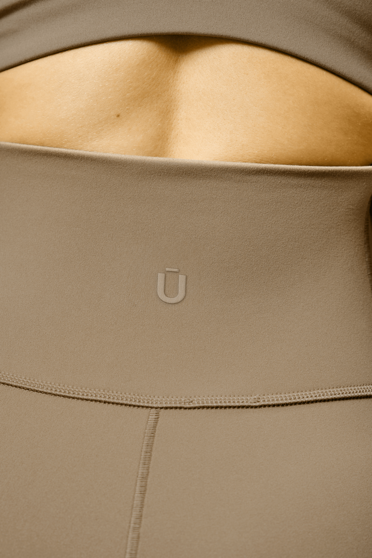 ŪKAIPŌ minimalist logo embossed on beige yoga pants showing elegant brand mark design