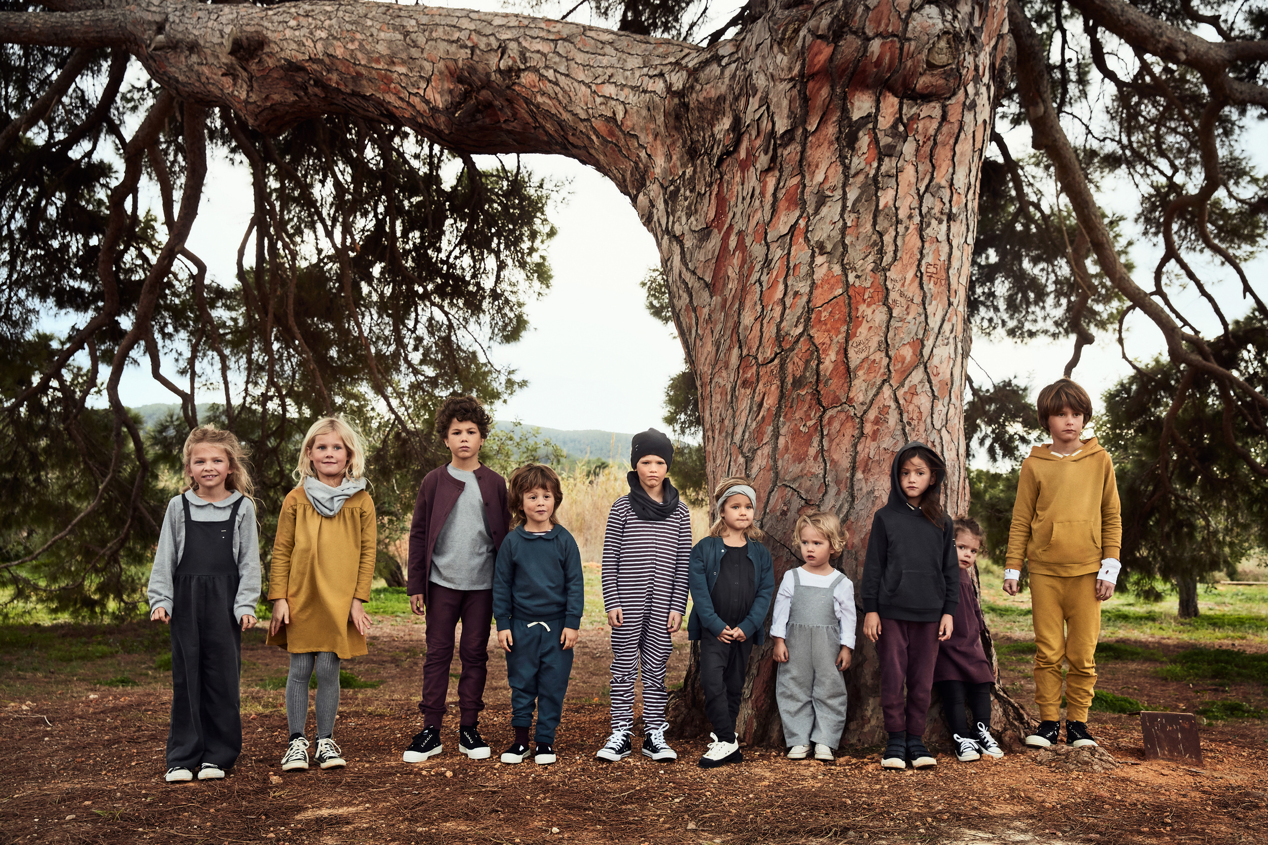 A group of ten children standing in front of a large tree in a natural setting.
