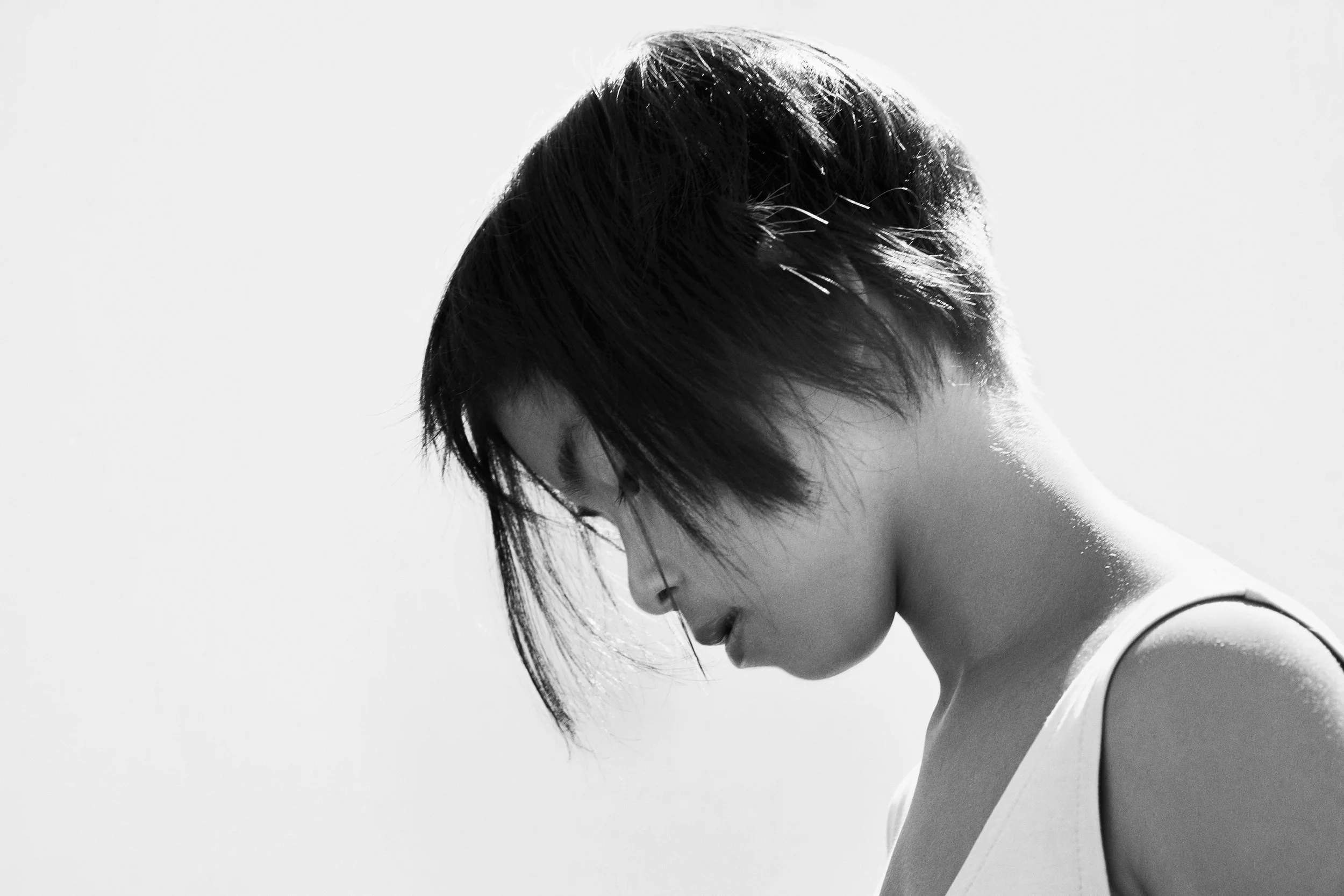 A side profile of a woman with short, dark hair, looking downward, in black and white.