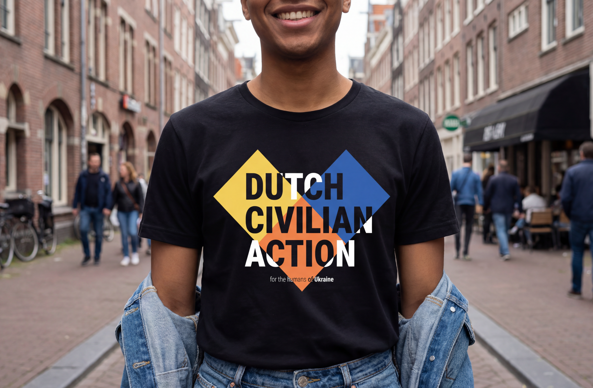 Person wearing a black T-shirt with the words "Dutch Civilian Action" and a message supporting Ukraine, standing in a city street with people walking in the background