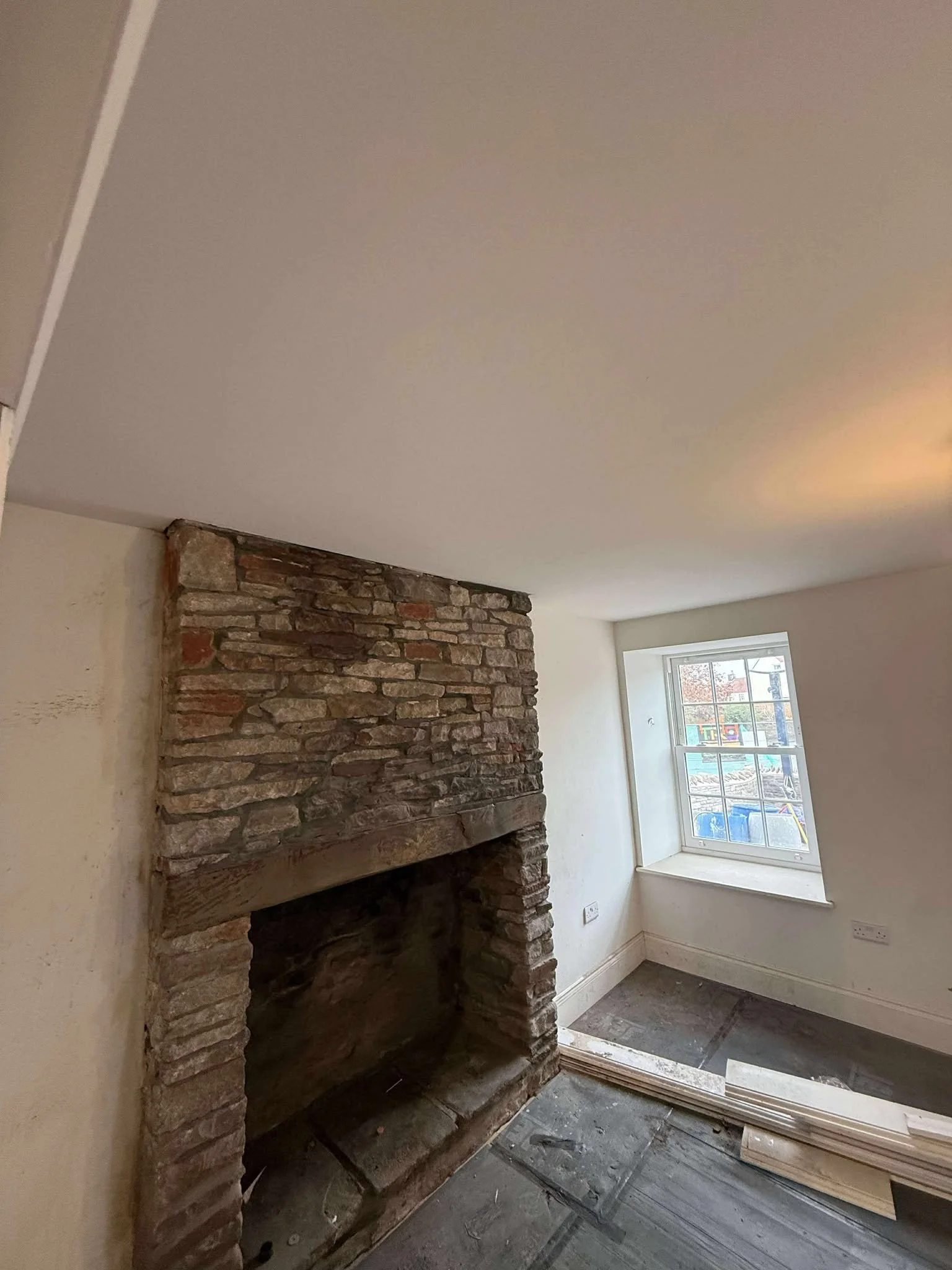 Empty room with exposed brick fireplace, large window, and construction materials on the floor.