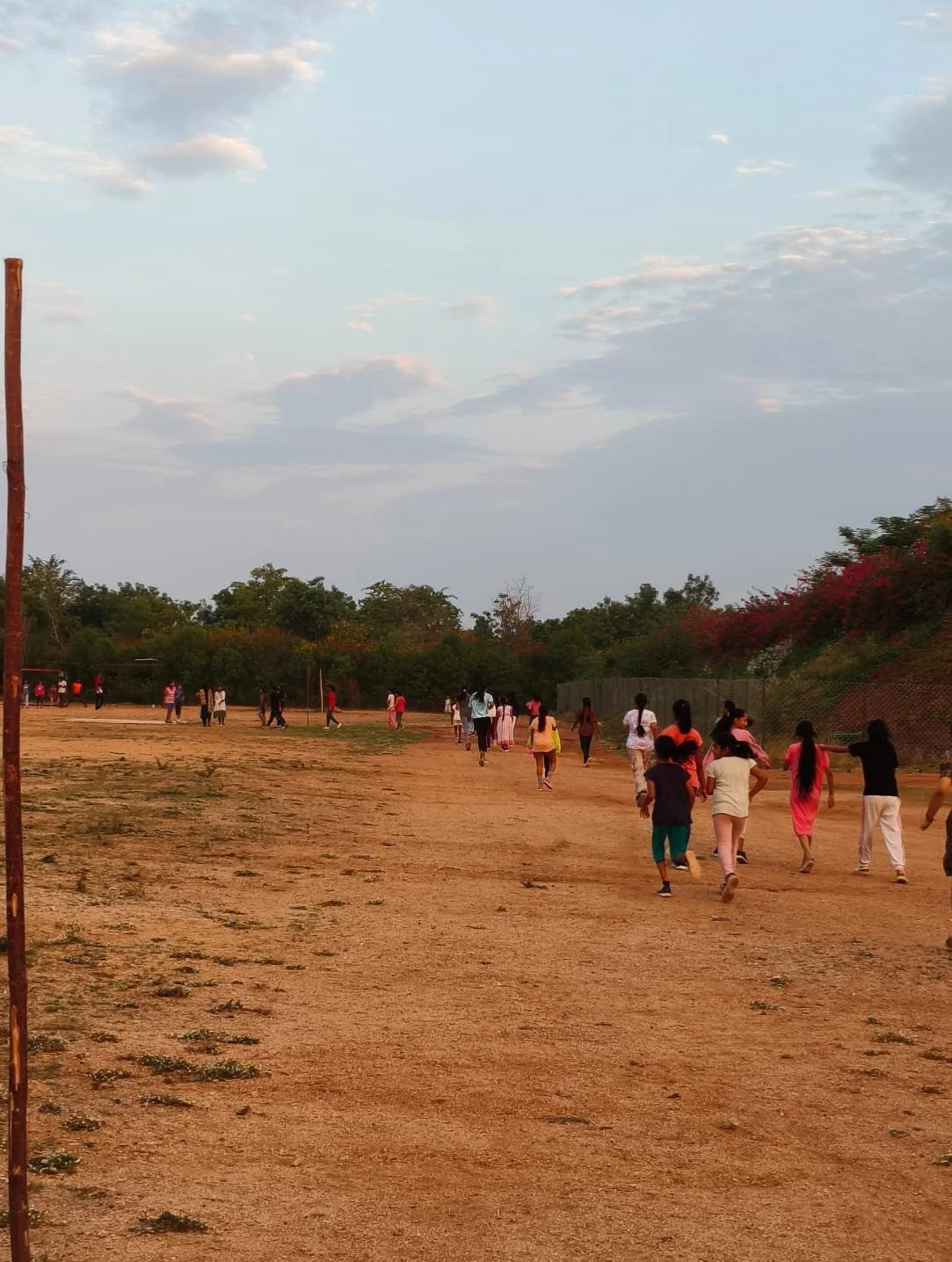 People walking on a dirt path in an open outdoor area with trees and bushes on the sides during the daytime.
