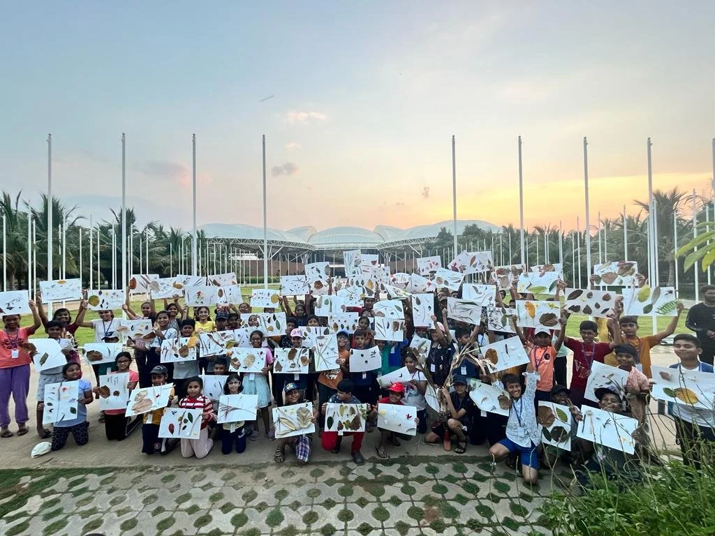 Group of children outdoors holding up drawings of leaves and plant parts during sunset.