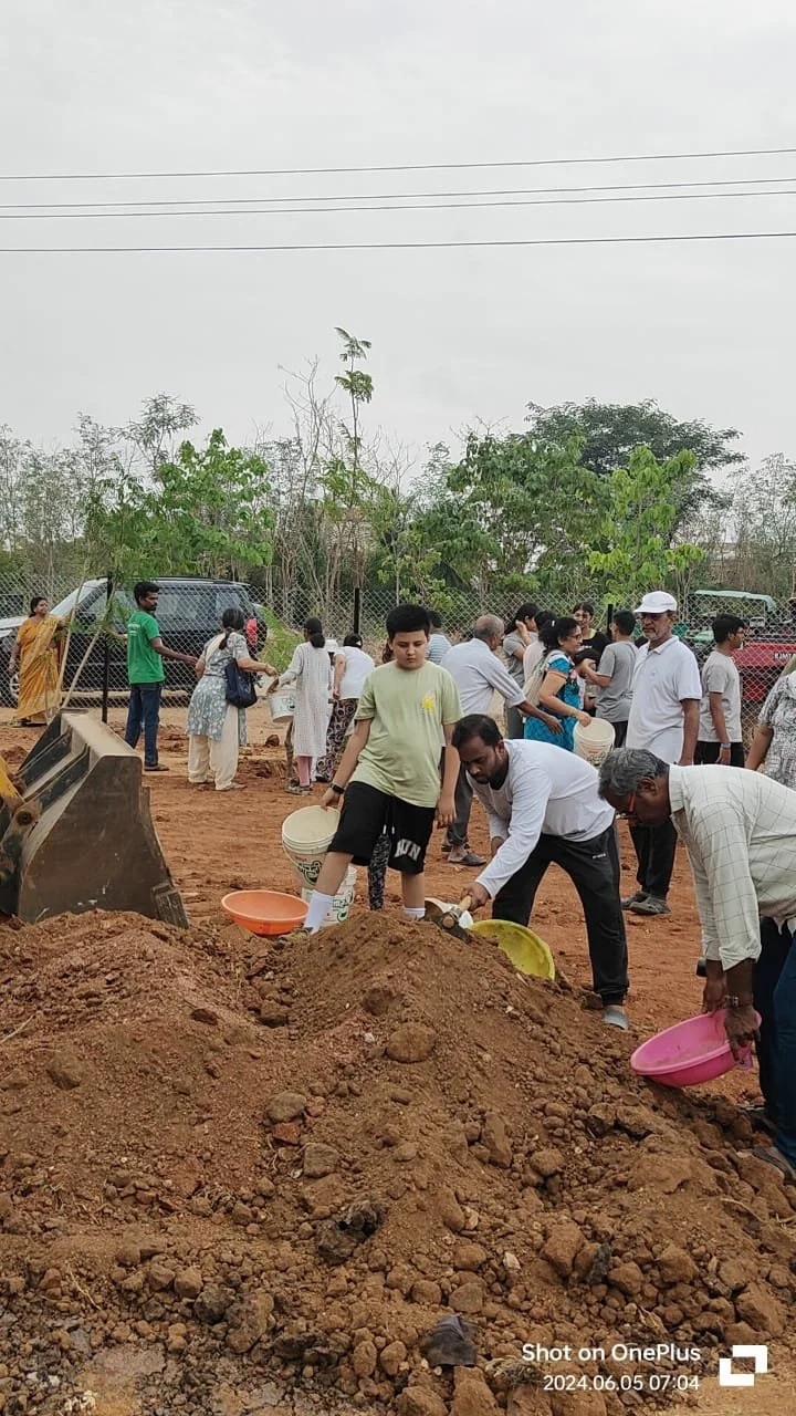 People gathered at a construction site filling buckets with soil, some standing in a line and others working near a large pile of dirt.