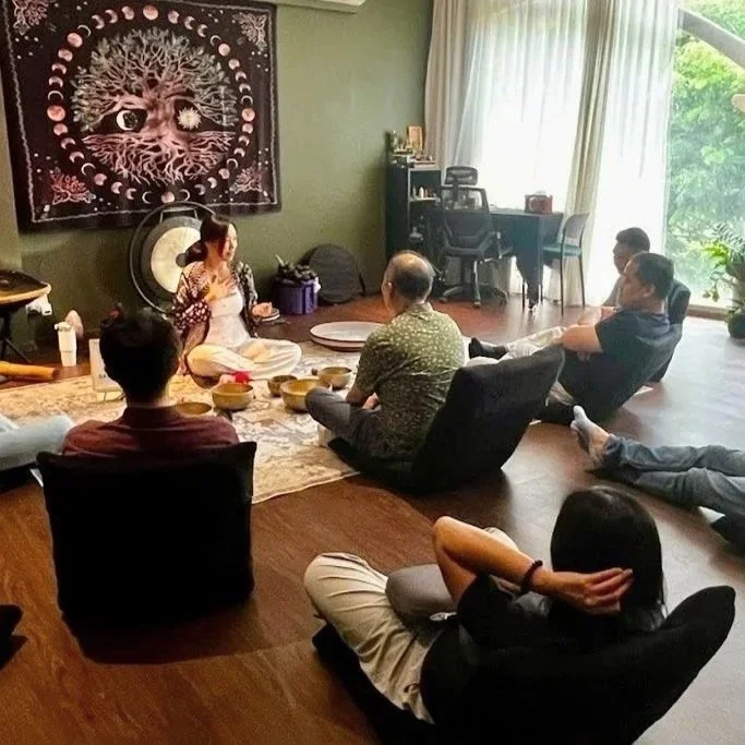 Person holding a Tibetan singing bowl and wooden mallet in a peaceful indoor setting, wearing a brown crochet shawl and bracelets.