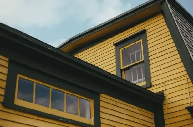 Yellow house exterior with dark trim, upper windows, and painted siding.