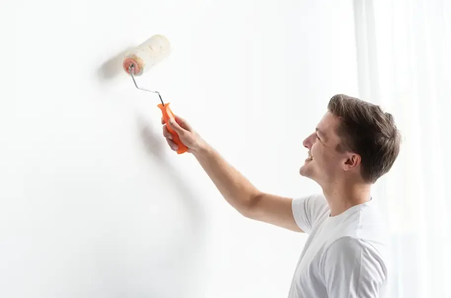 A man painting a wall with white paint while smiling - Stephen Radl Painting