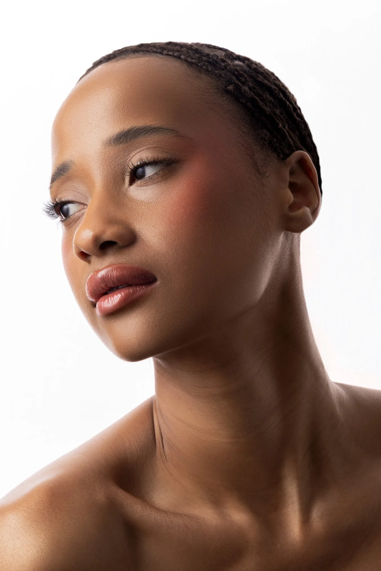 Un portrait en gros plan d'une femme noire avec peau lumineuse, coiffée de petites tresses, regardant légèrement vers la gauche, contre un fond blanc.