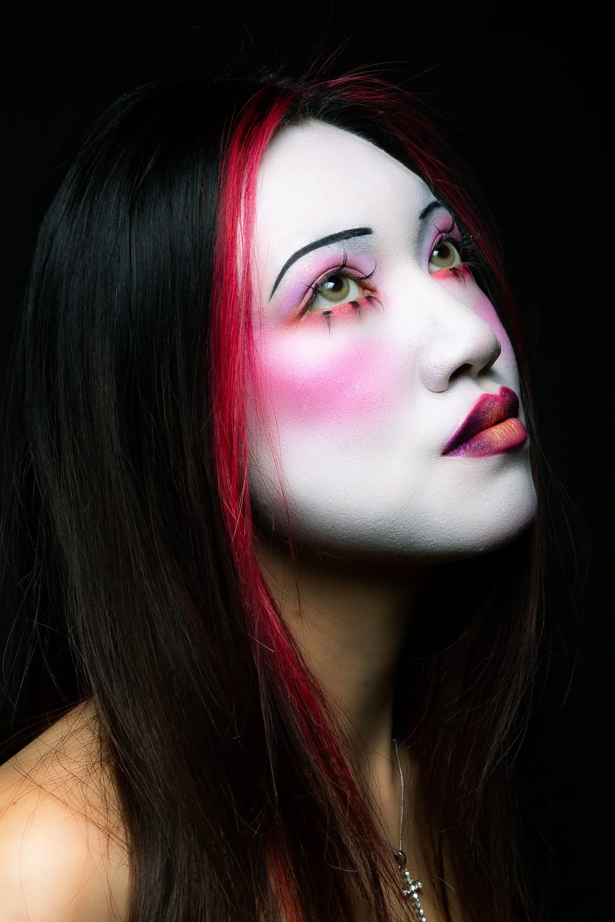 Portrait d'une femme avec maquillage artistique, cheveux noirs avec des mèches rouges, fond noir.