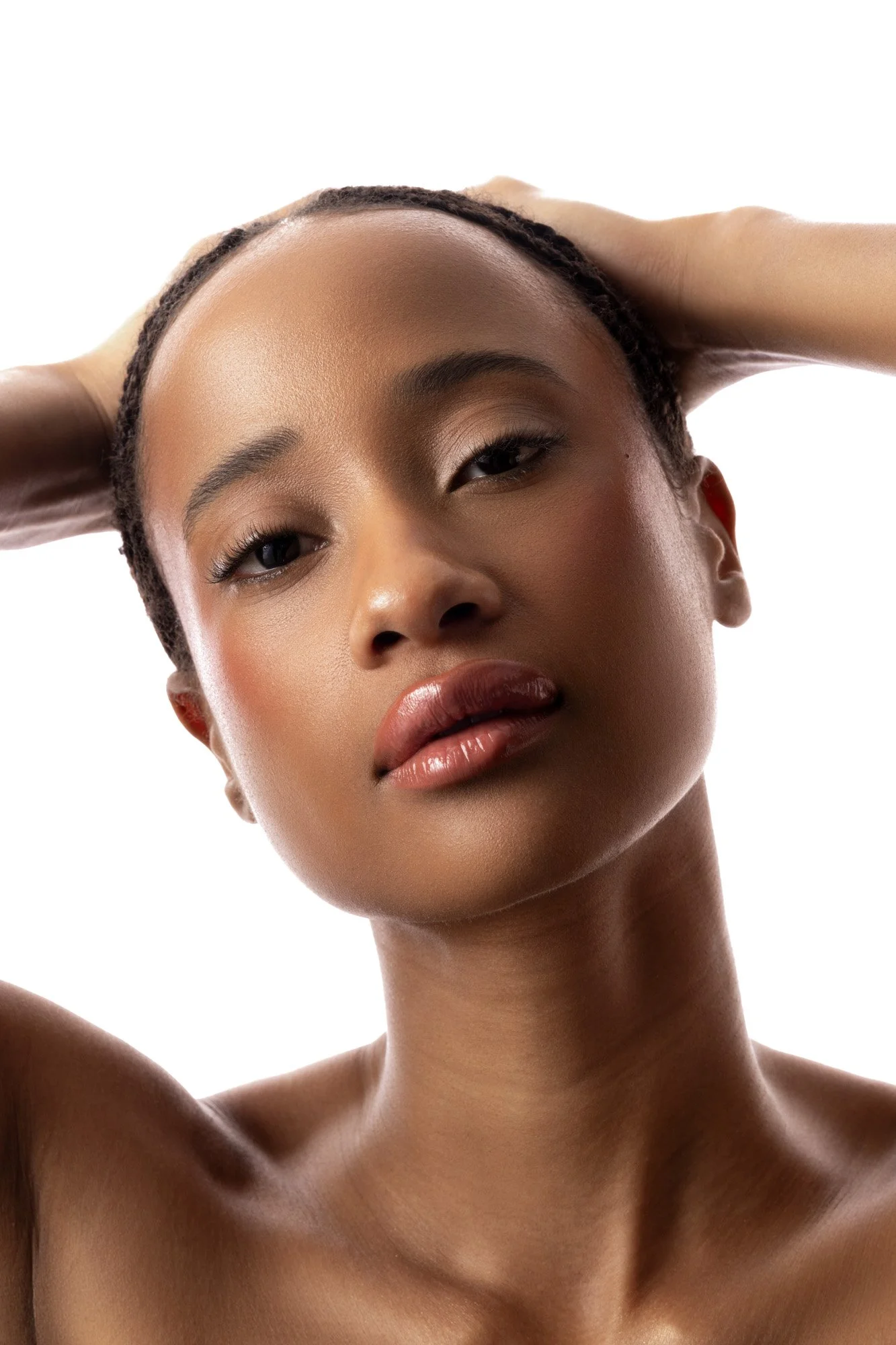 Jeune femme noire avec une peau lisse et naturelle, visage expressif, mains derrière la tête, fond blanc
