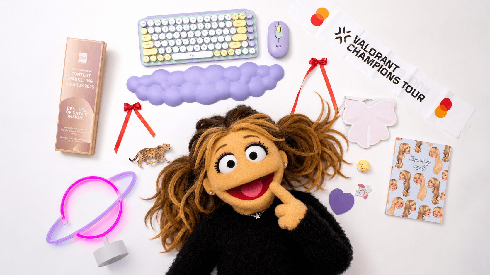 A puppet character with brown hair, wearing a black shirt and a necklace with a letter K, stands in front of a high-tech control room with digital screens and graphs.