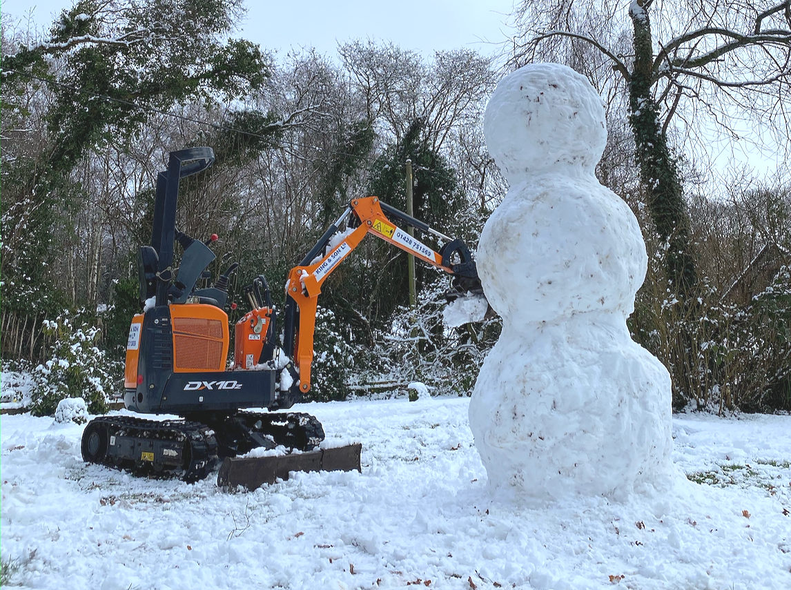Mini excavator carving a snowman in a snowy yard.