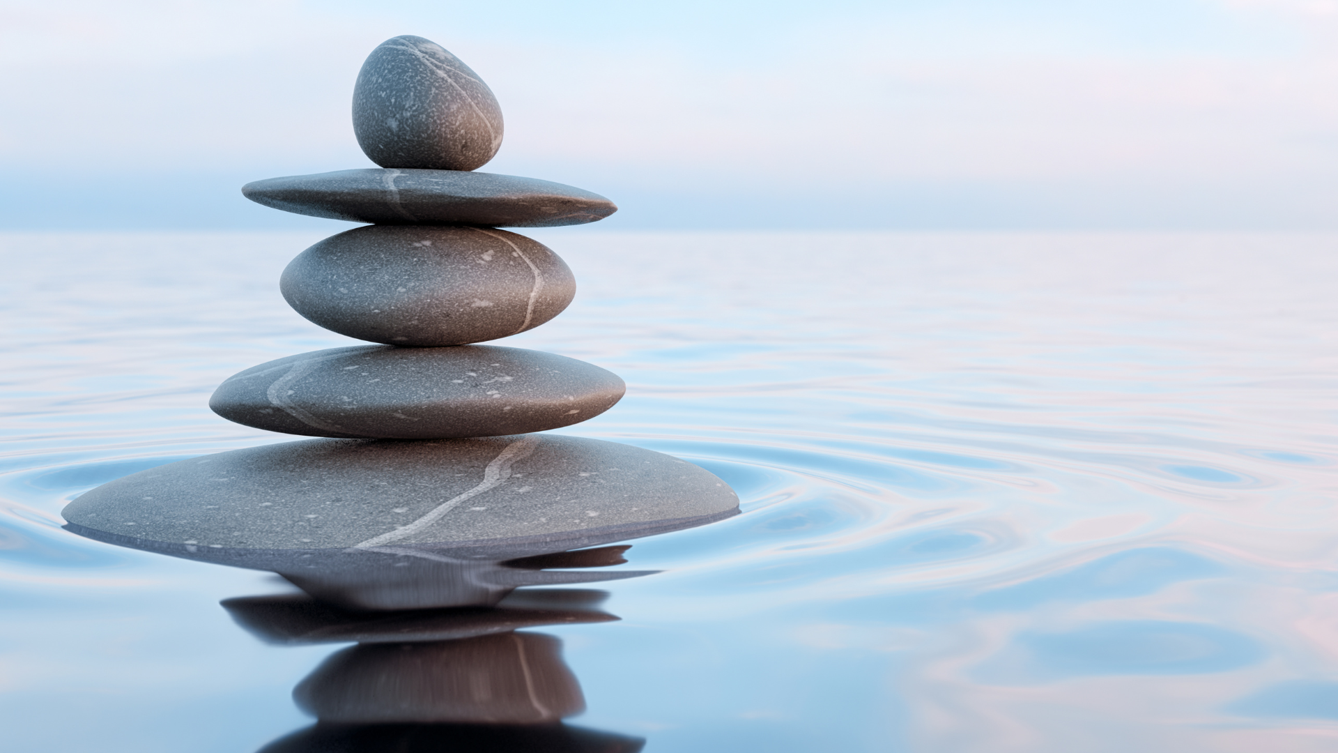 A calm scene featuring five smooth grey stones stacked in a balancing tower.
